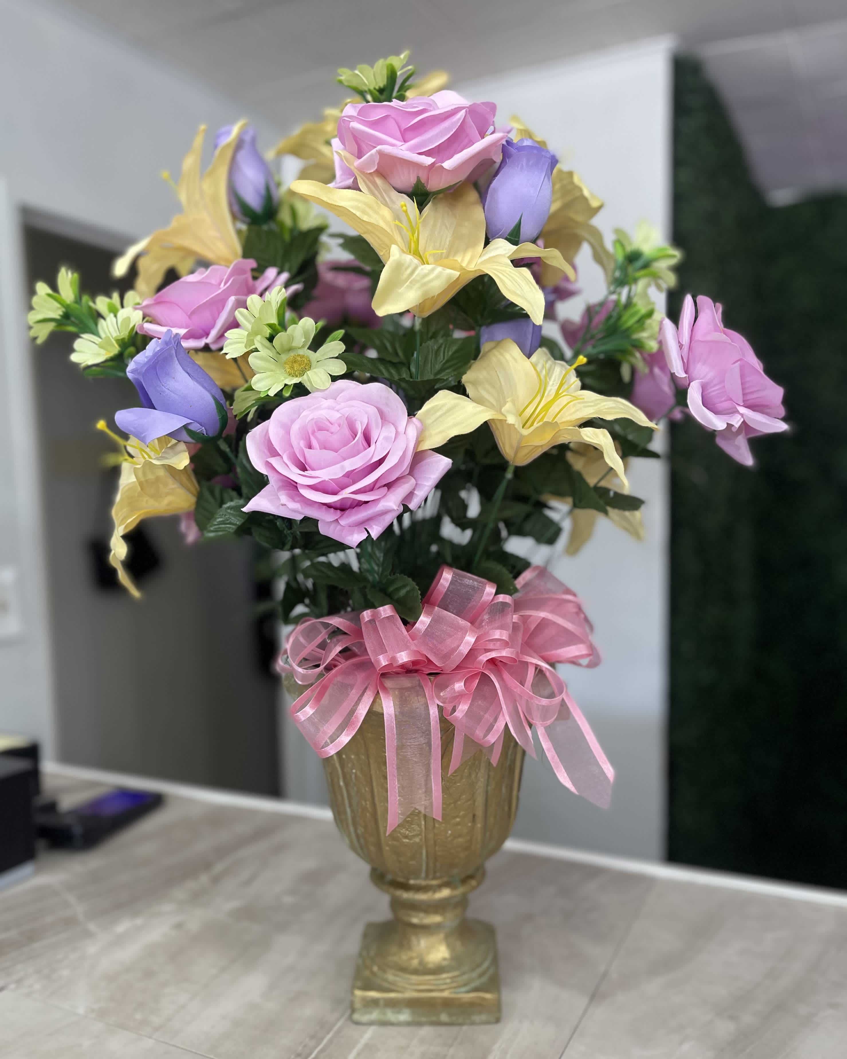 Pink and yellow floral arrangement in a gold vase with a pink ribbon bow