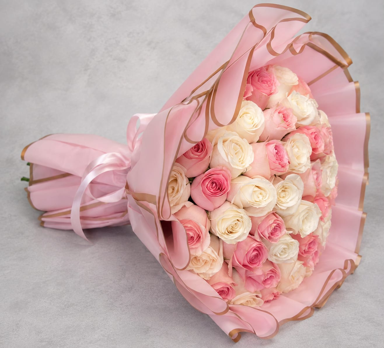 Bouquet of pink and white roses wrapped in pink paper with ribbon