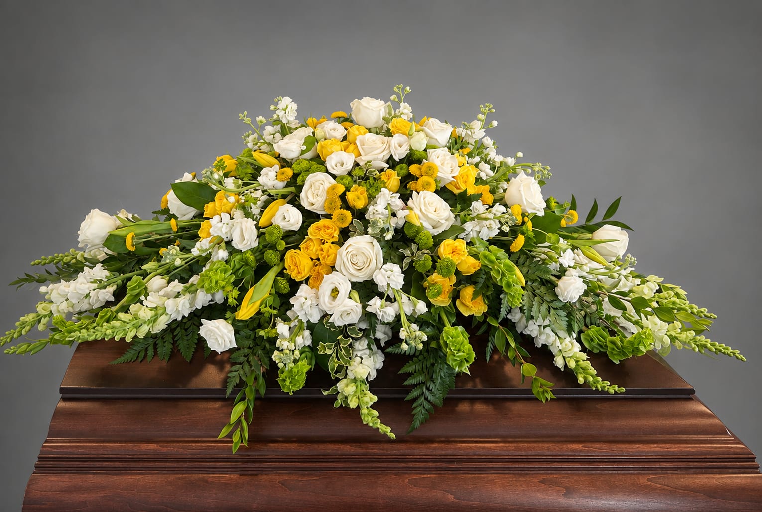 White and yellow floral casket spray on a wooden casket
