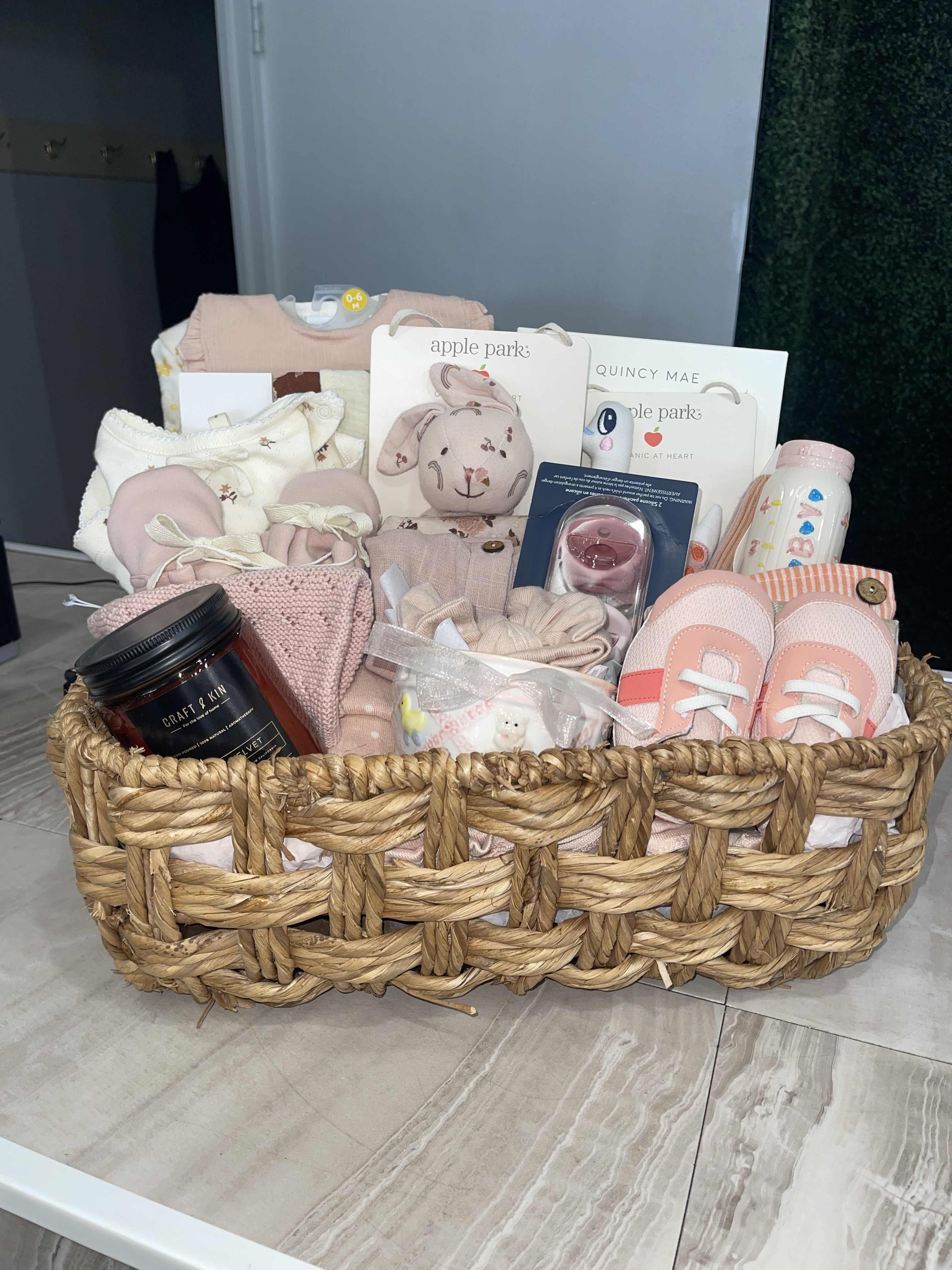 Gift basket with baby clothes, toys, and accessories in a woven basket