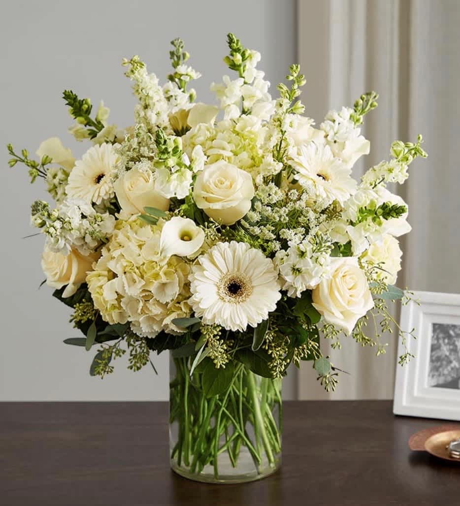 Creamy white bouquet in a clear glass vase with roses, gerberas, and snapdragons