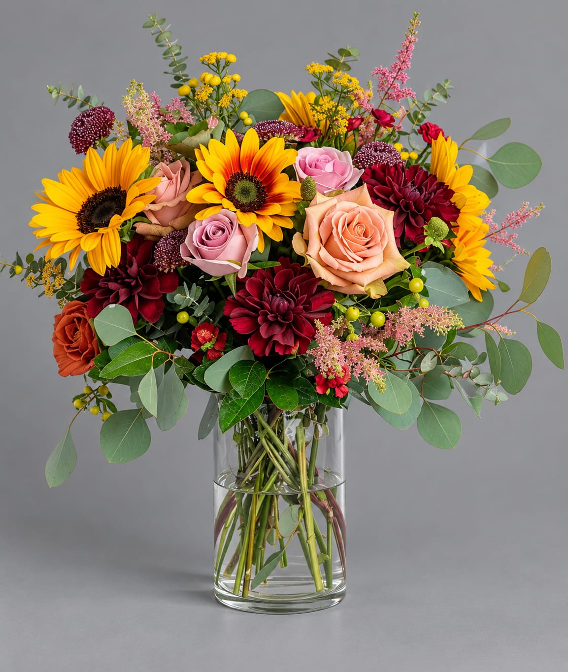 Mixed bouquet of sunflowers, roses, and dahlias in a glass vase