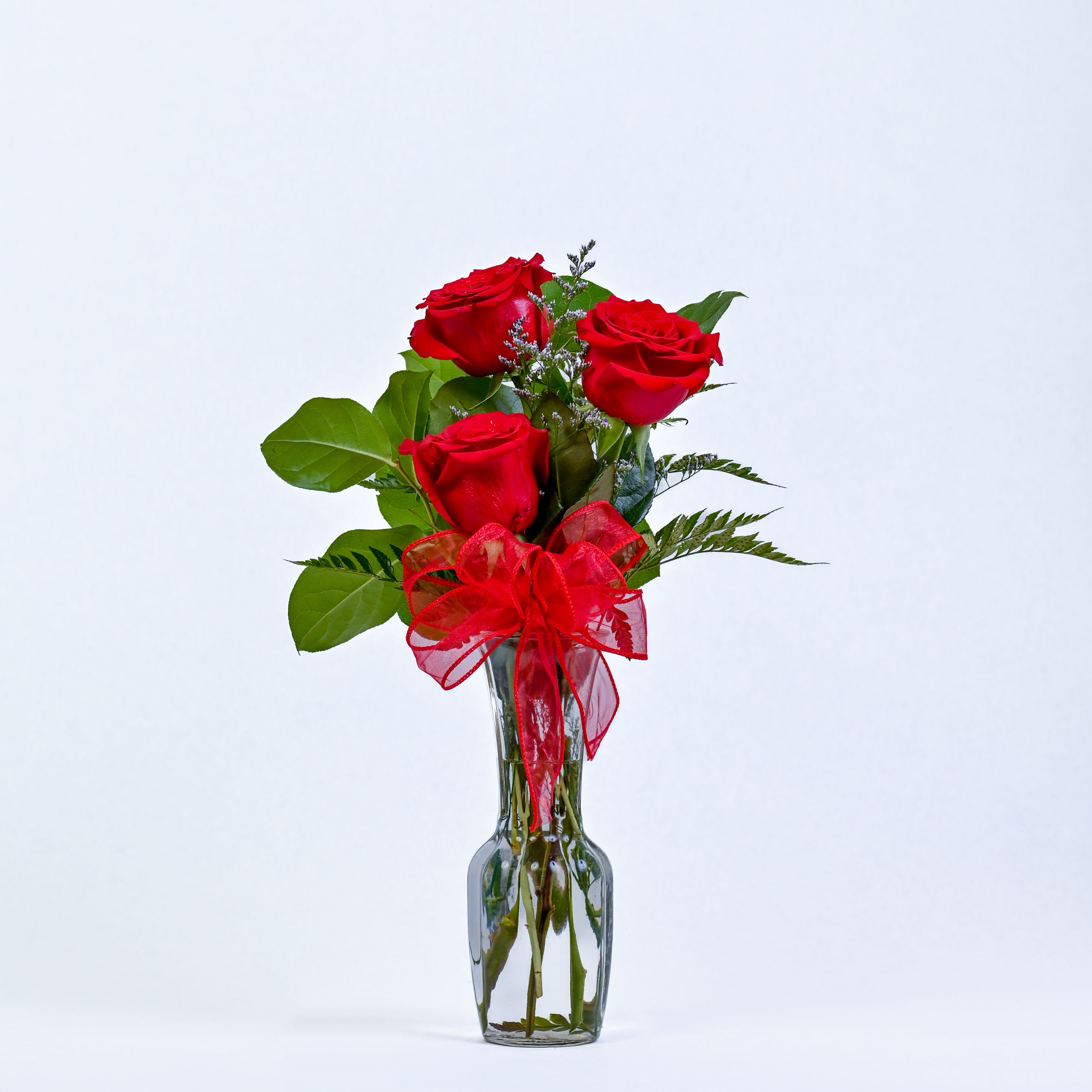 Three red roses in a clear glass vase with a red ribbon