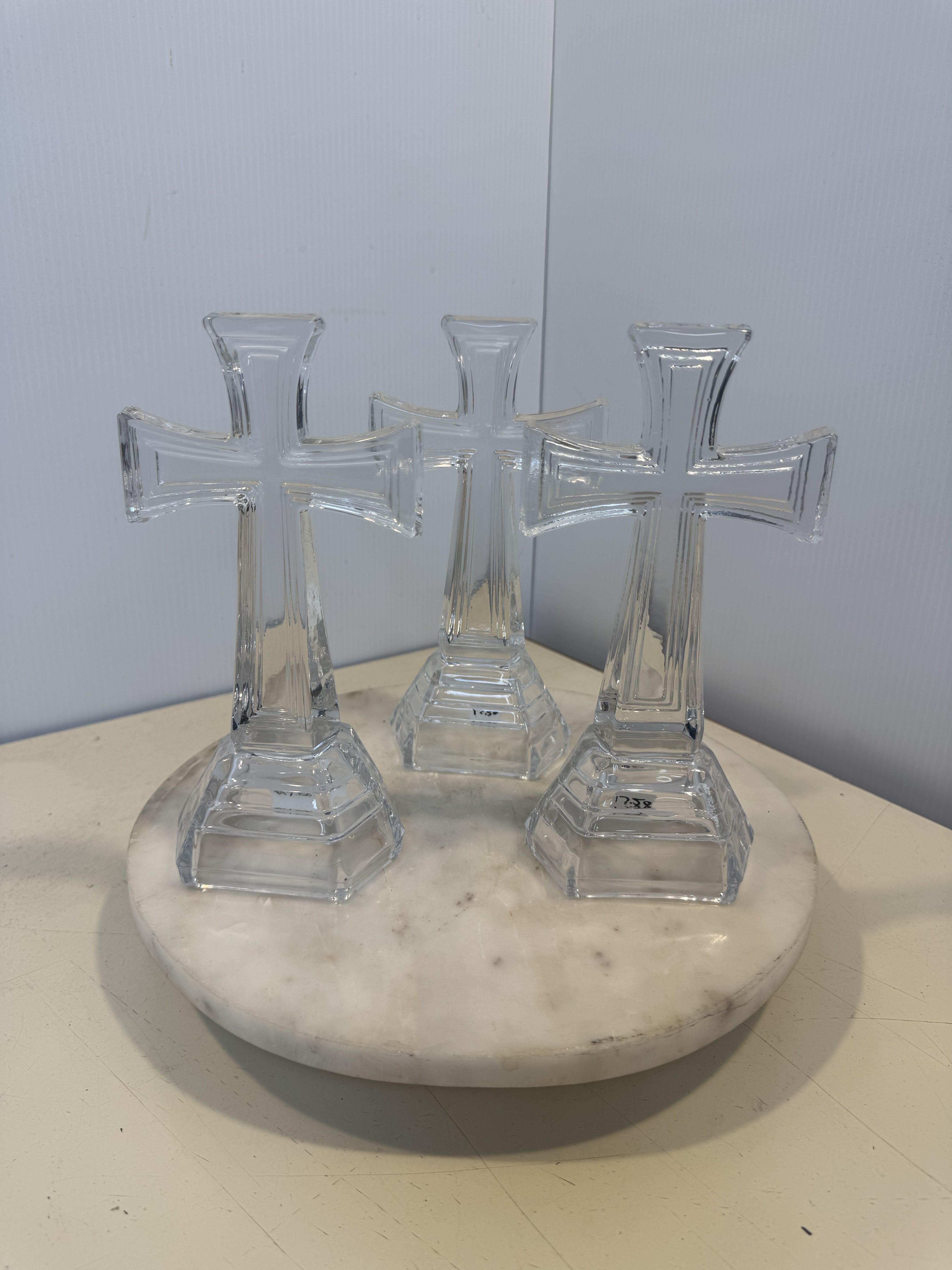 Three clear glass cross-shaped ornaments on a round white base