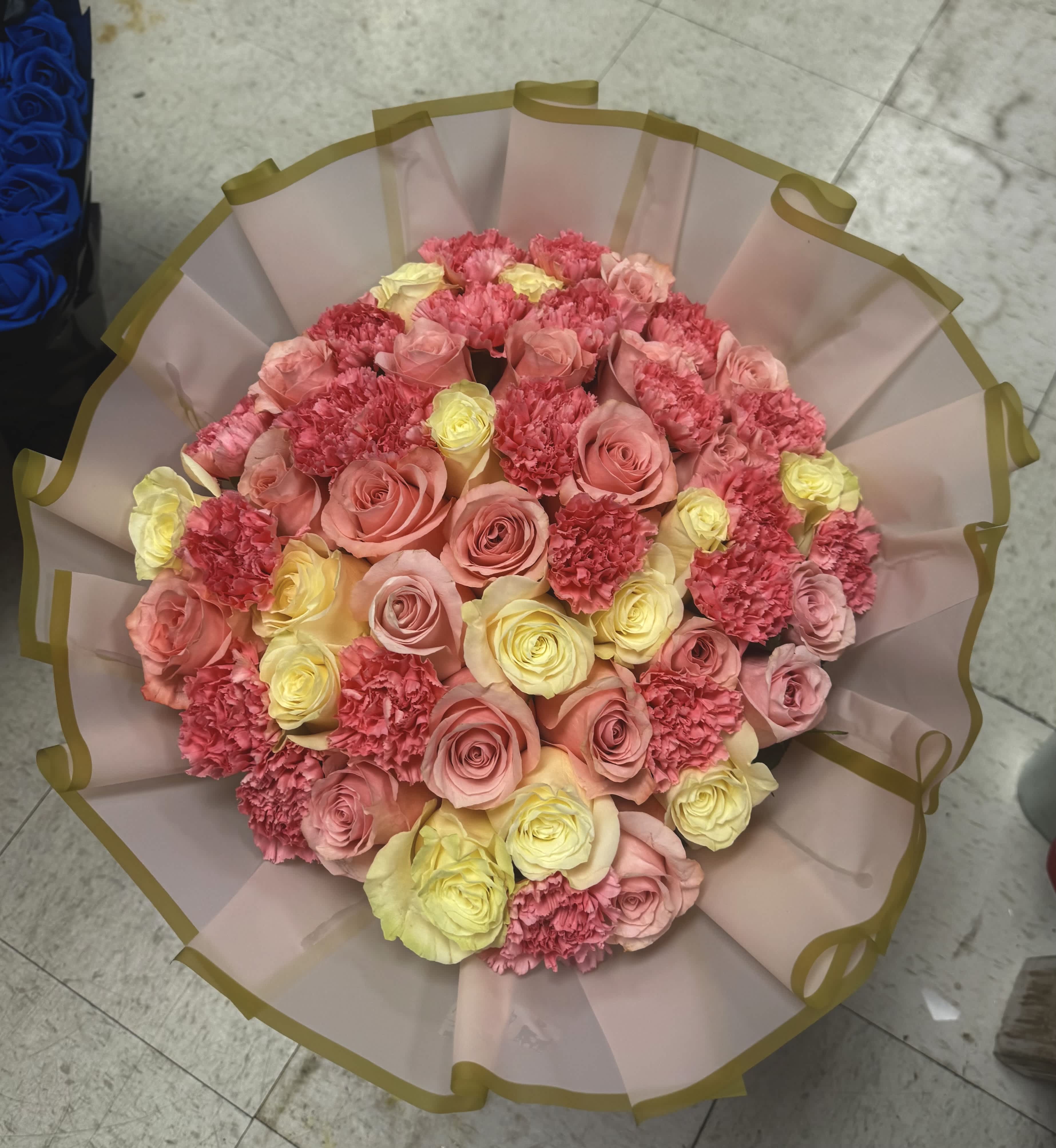 Round bouquet of pink and yellow roses with carnations in pale wrapping