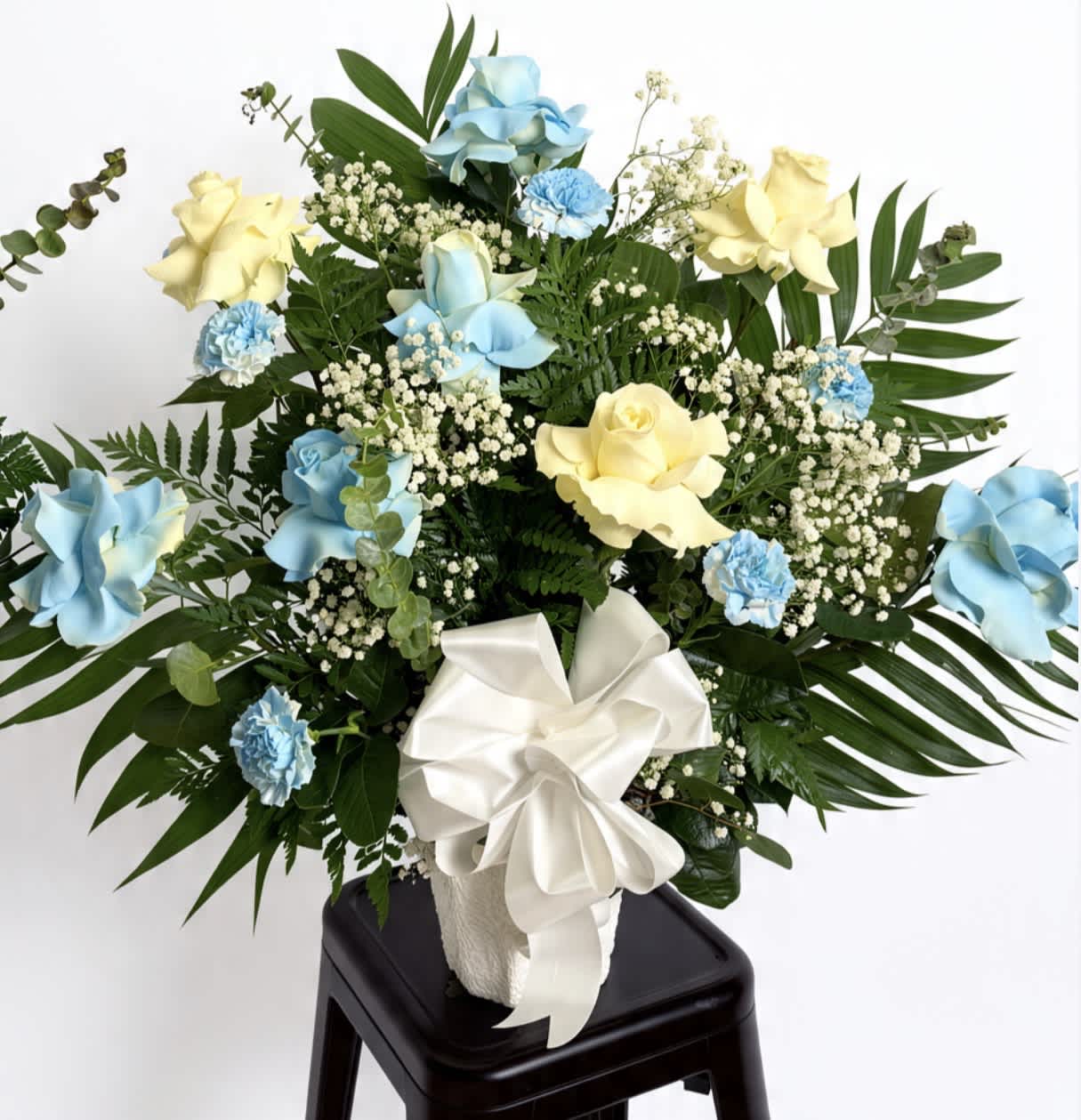 Blue and yellow rose arrangement with white ribbon in a vase