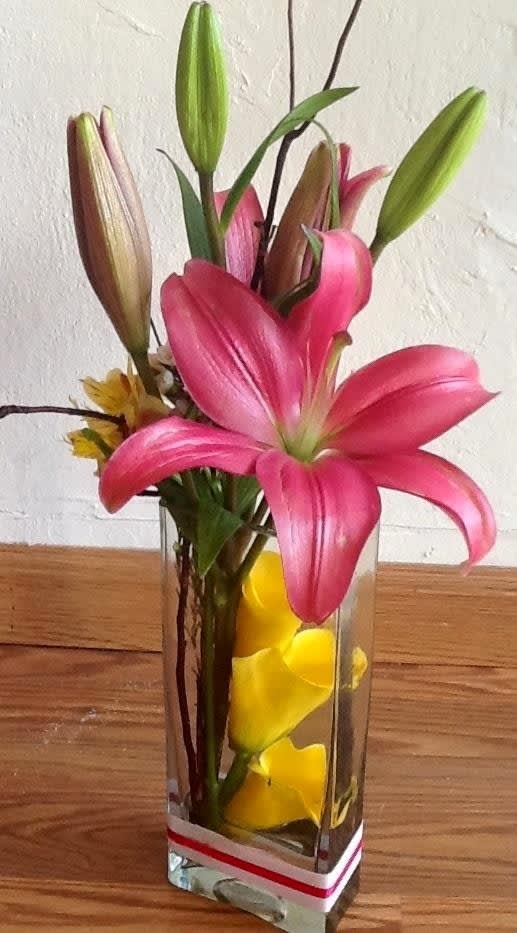 Pink lilies in a clear rectangular vase with yellow petals inside