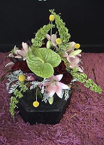 Floral arrangement in a black container with pink lilies and green accents
