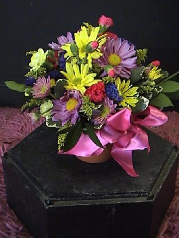 Mixed bouquet of purple, yellow, and pink flowers with a pink ribbon