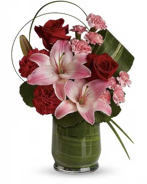 Pink lilies and red roses arranged in a green glass vase