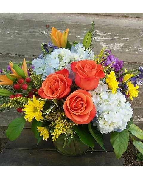 Bouquet of orange roses, blue hydrangeas, and yellow daisies in a vase