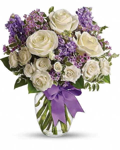 White roses and purple flowers in a glass vase with a purple ribbon