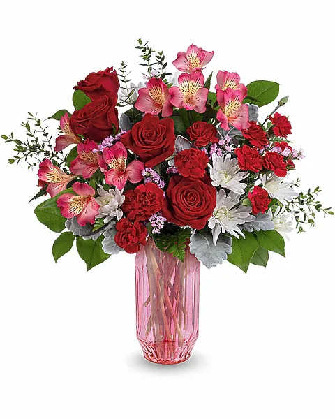 Bouquet of red roses and pink flowers in a pink glass vase