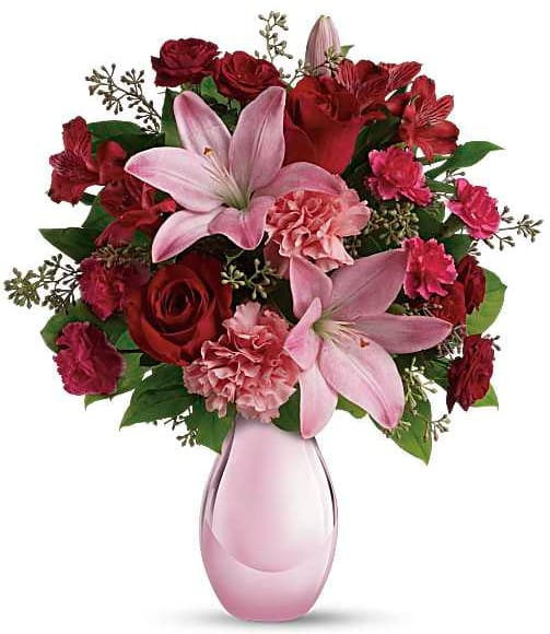 Pink lilies and red roses arranged in a pink glass vase