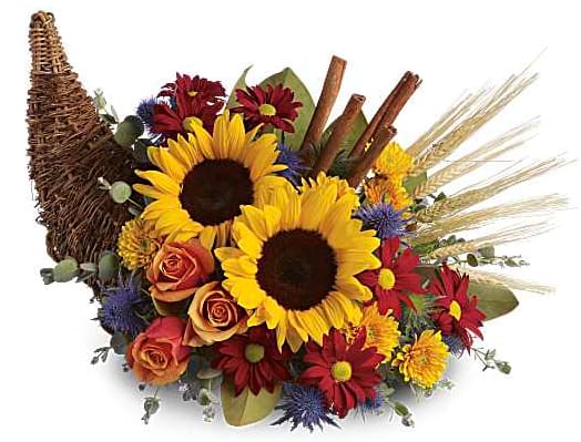 Sunflowers and mixed blooms arranged with wheat and cinnamon sticks in a wicker cornucopia