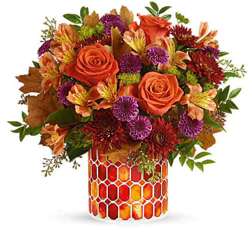 Orange roses and mixed fall flowers in a patterned glass vase