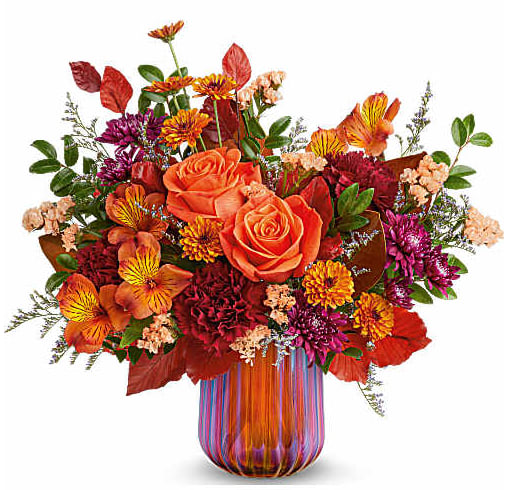 Orange roses and mixed fall flowers in a striped glass vase