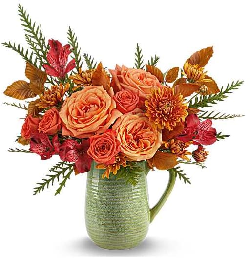 Orange and red floral arrangement in a green ceramic pitcher vase