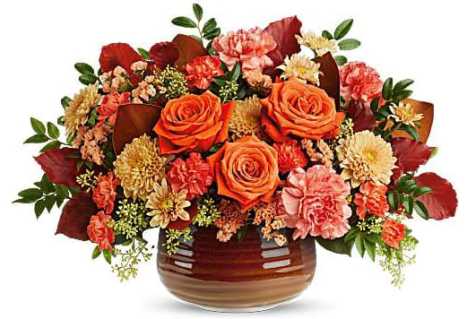 Orange roses and mixed fall flowers arranged in a brown ceramic vase