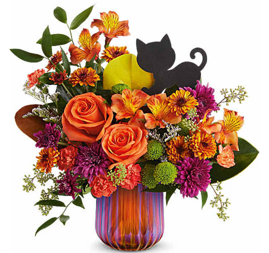 Orange and purple flower arrangement in a striped glass vase with a black cat decoration