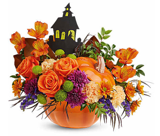 Orange floral arrangement in a pumpkin container with a haunted house topper