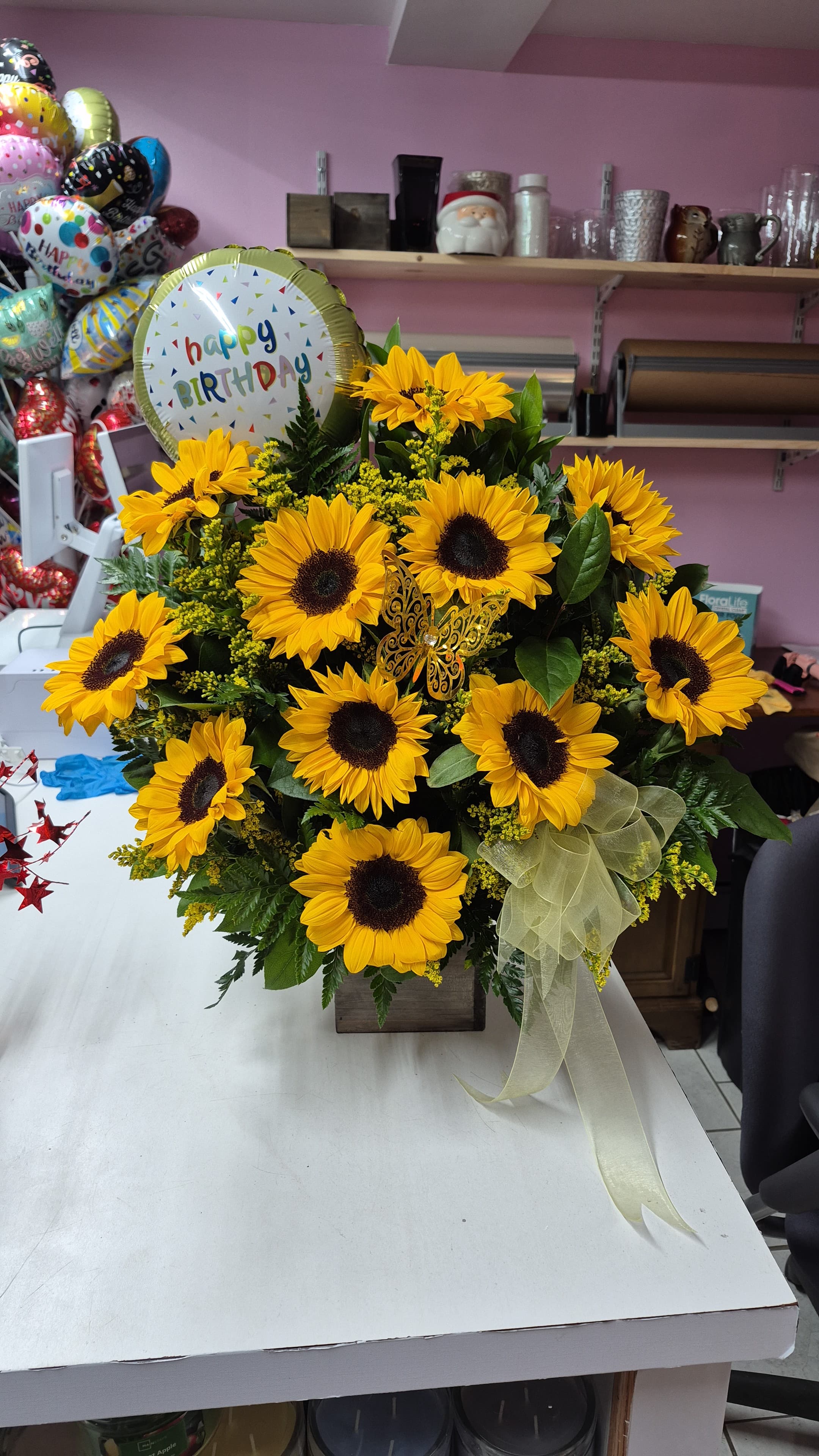Sunflower arrangement with a birthday balloon and ribbon in a wooden container.