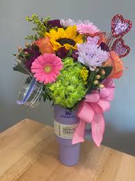 Colorful bouquet with a sunflower, gerbera daisies, and a pink ribbon in a purple vase