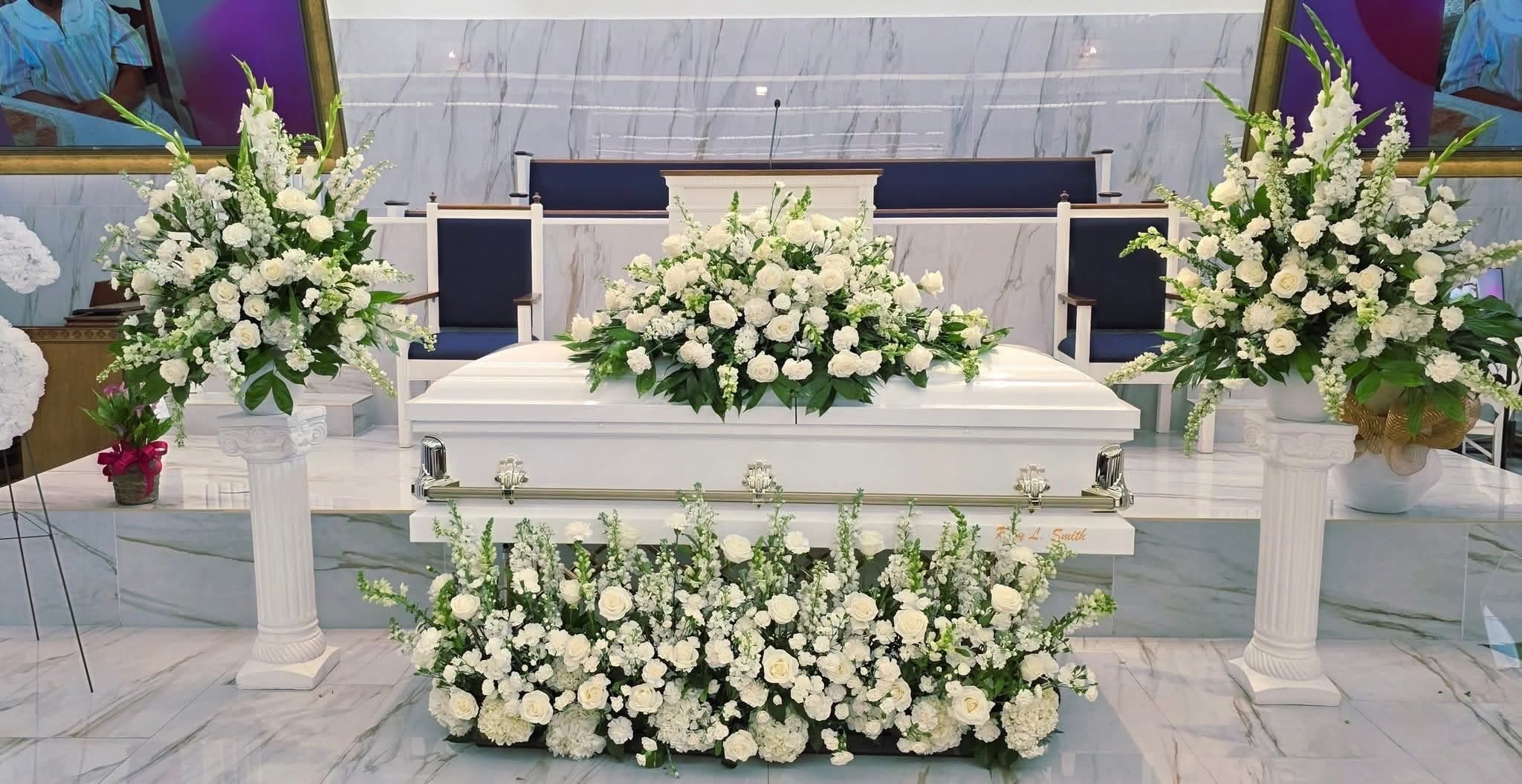 White floral funeral spray arranged around a white casket
