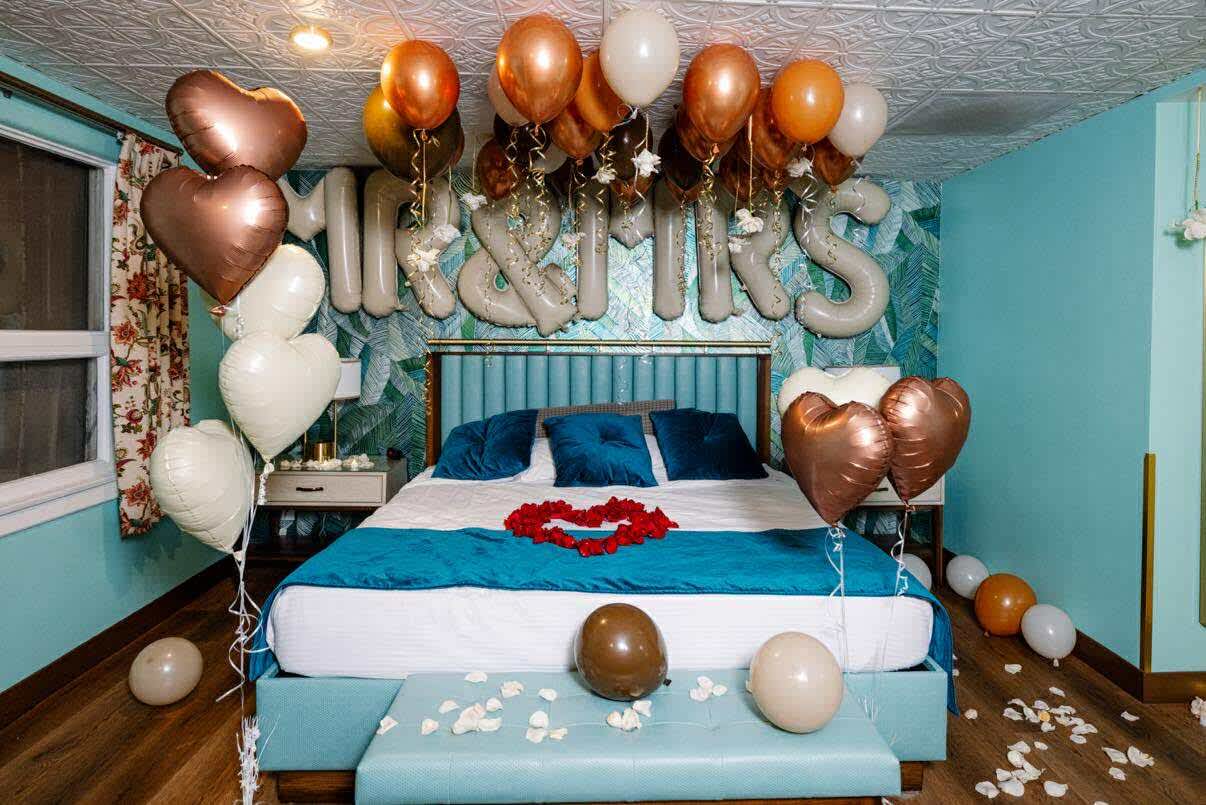 Bedroom decorated with heart-shaped balloons and rose petals on the bed