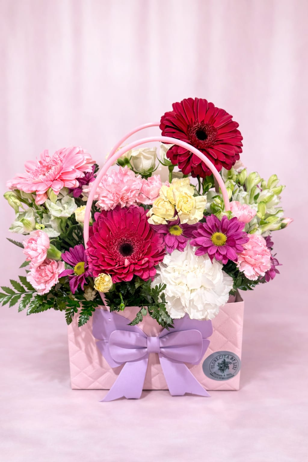Pink gift bag filled with mixed flowers and a lavender bow