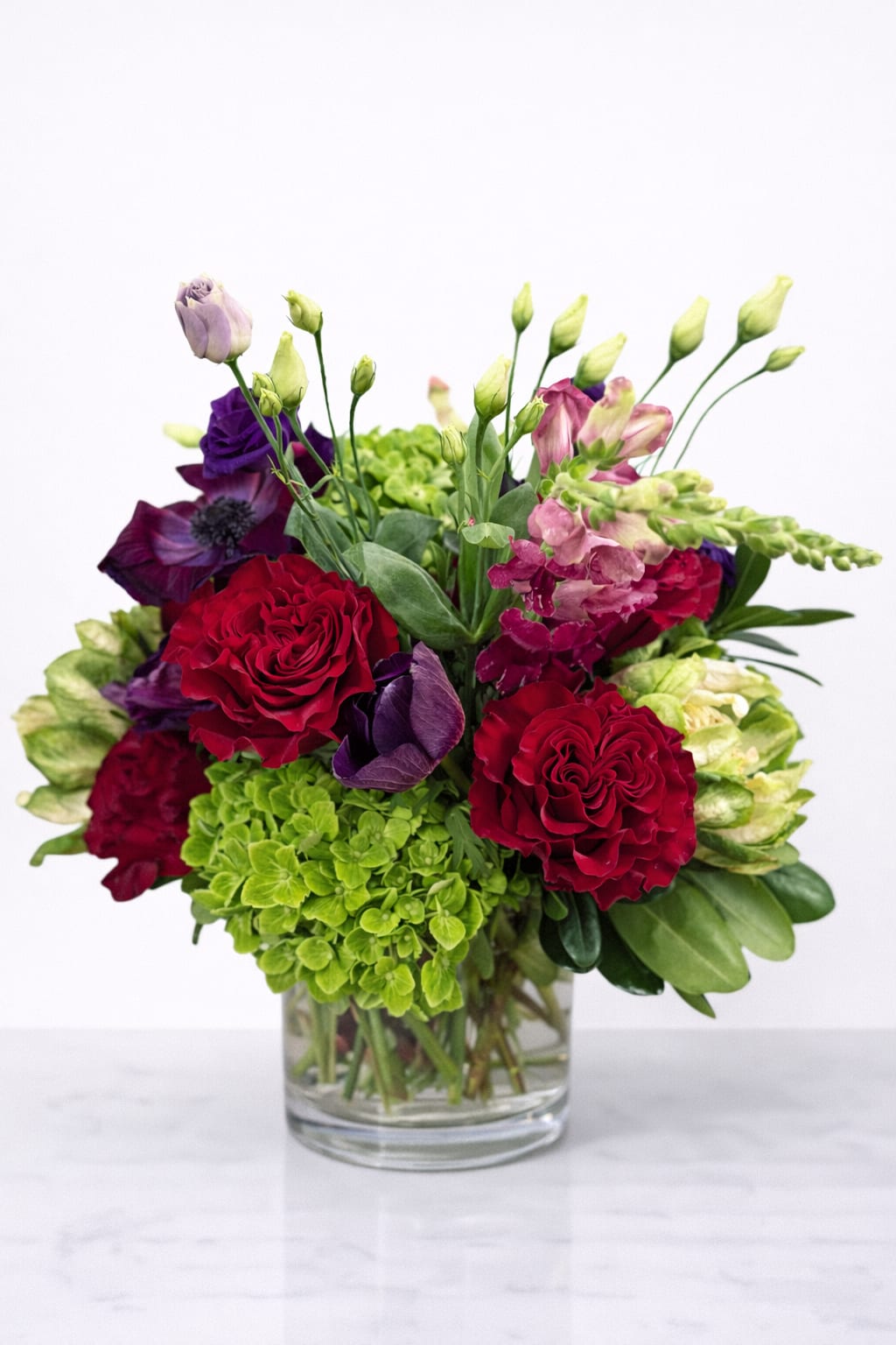 Amethyst - Rich, dimensional, and quietly powerful, Amethyst is a statement in contrast and confidence. Velvety crimson roses, inky purples, and lush green hydrangea unfold with sculptural movement and unexpected texture. Designed to feel both intimate and commanding, this arrangement brings a sense of luxury, confidence, and modern romance to any space. A cornerstone of our Valentine's Day collection.
