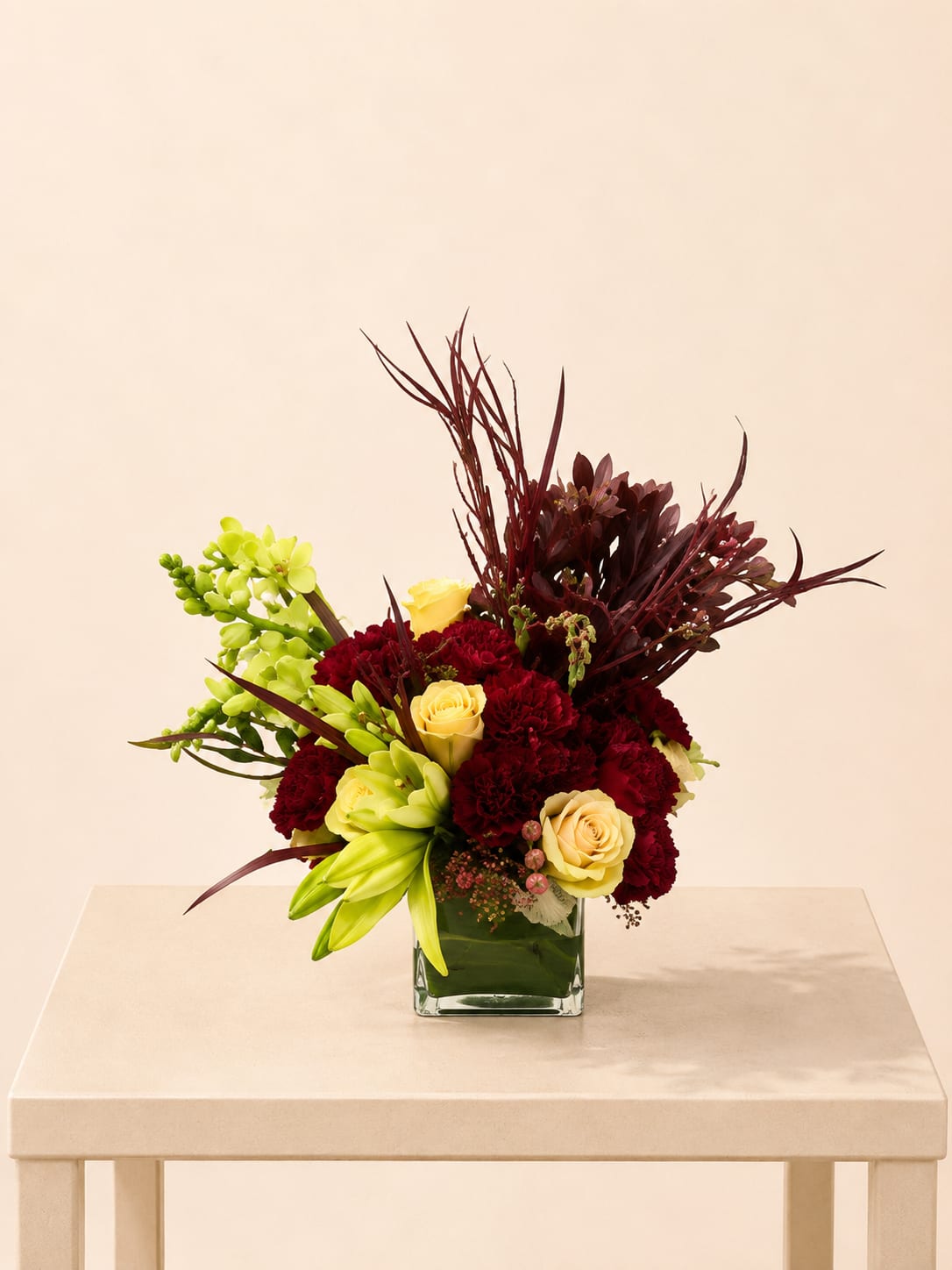 Bouquet of red carnations, yellow roses, and green orchids in a square glass vase