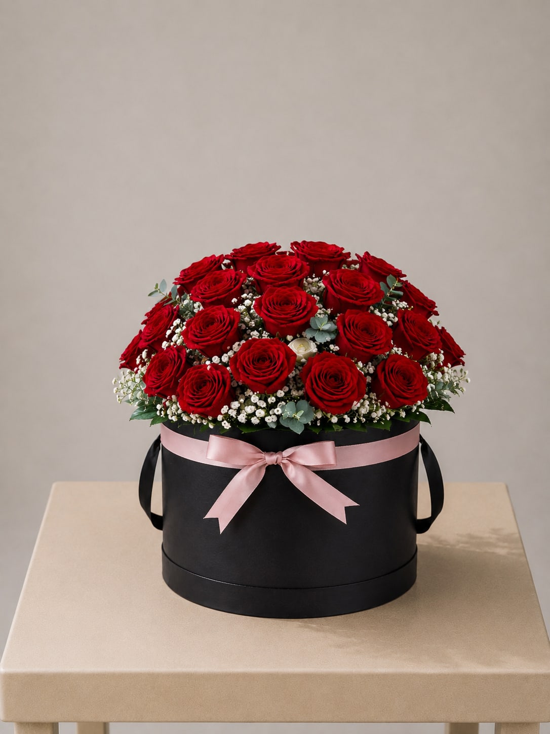 Red roses arranged in a black round box with a pink ribbon