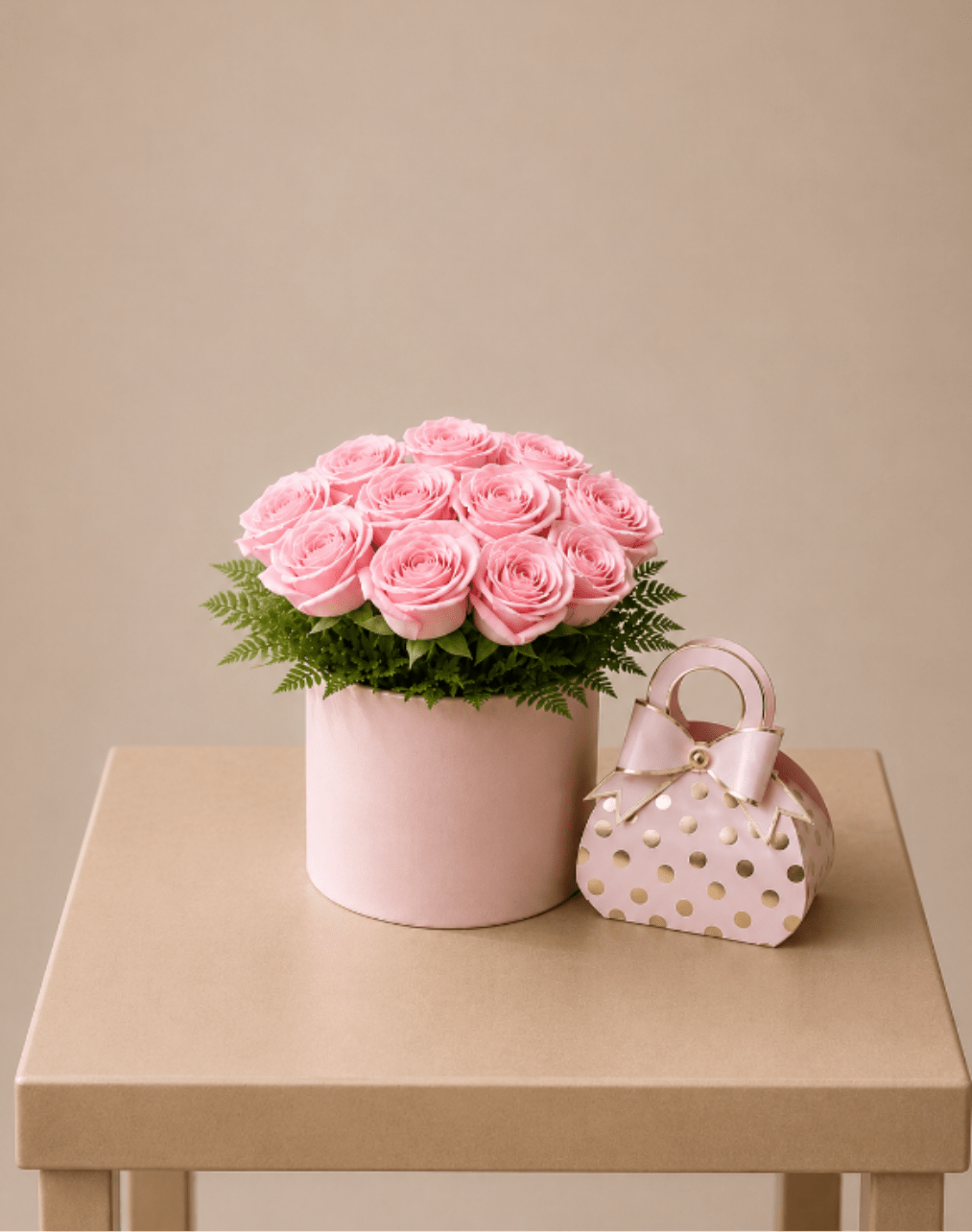Pink roses in a round box with a small polka-dot gift bag beside it