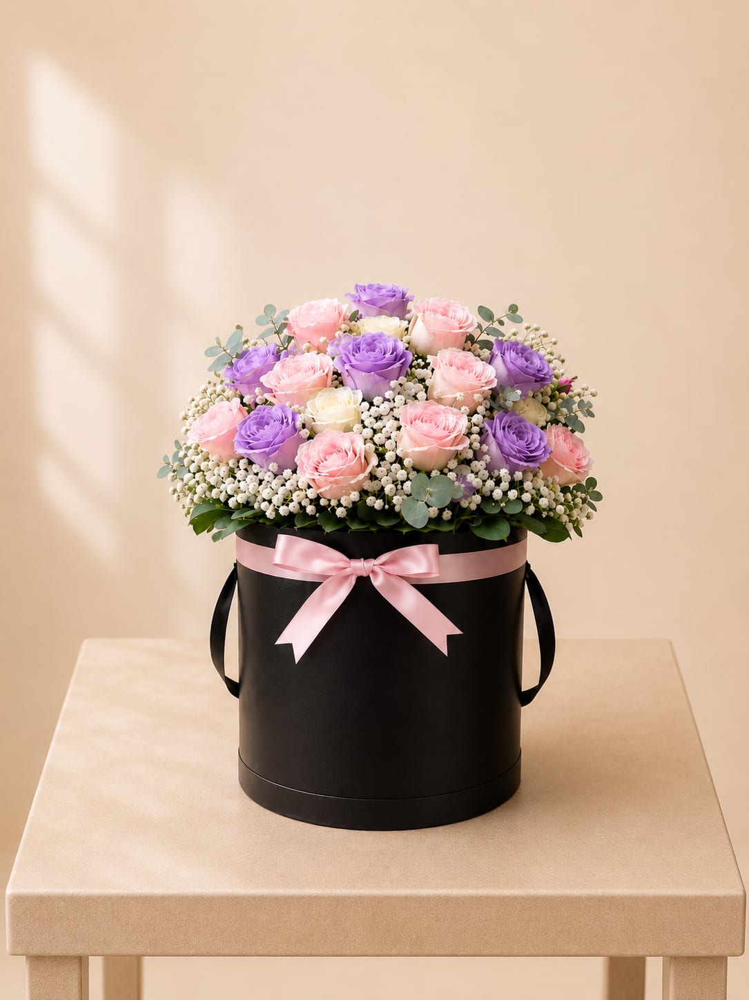 Pastel Garden Rose Hatbox – Tall - An elegant flower arrangement featuring 24 roses in soft blush, lavender, and ivory tones, accented with delicate white blooms and fresh greenery. Beautifully designed in a tall black hatbox and finished with a soft blush ribbon, this design offers a refined and romantic statement with timeless appeal.  Perfect for Mother’s Day, birthdays, anniversaries, sympathy, or a meaningful and elegant “just because” surprise.  Available for local flower delivery throughout Naples, Bonita Springs, Estero, Fort Myers and Fort Myers Beach.  Designer’s Choice: Each arrangement is uniquely designed using the freshest seasonal flowers available. Flower varieties, colors and containers may vary while maintaining the overall style, value and beauty of the design.