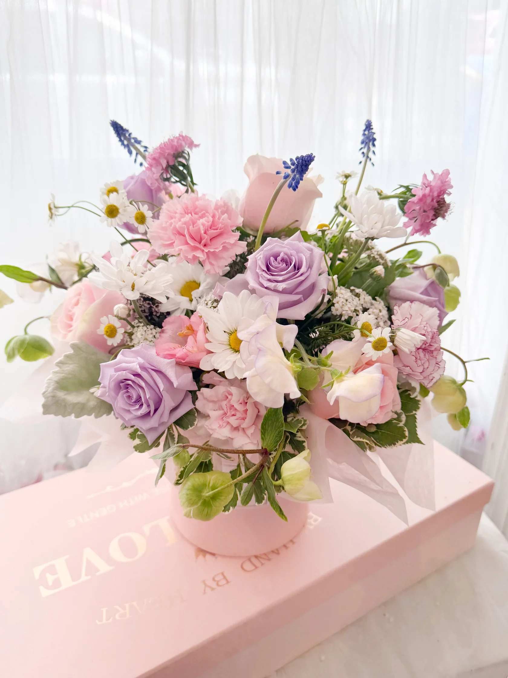 Pink and lavender bouquet with roses, carnations, and daisies in a round box