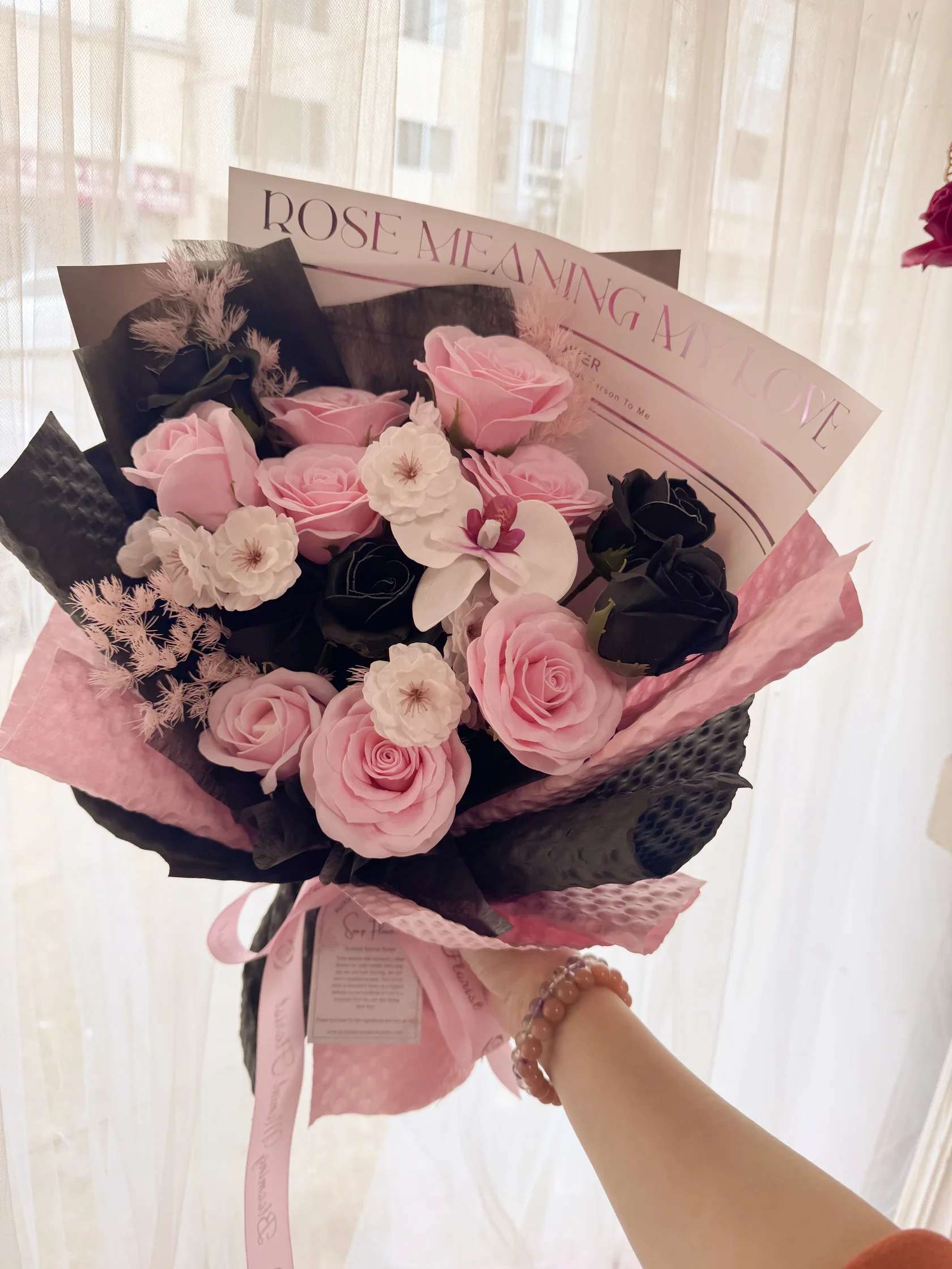 Pink and black rose bouquet with white accent flowers and decorative wrapping