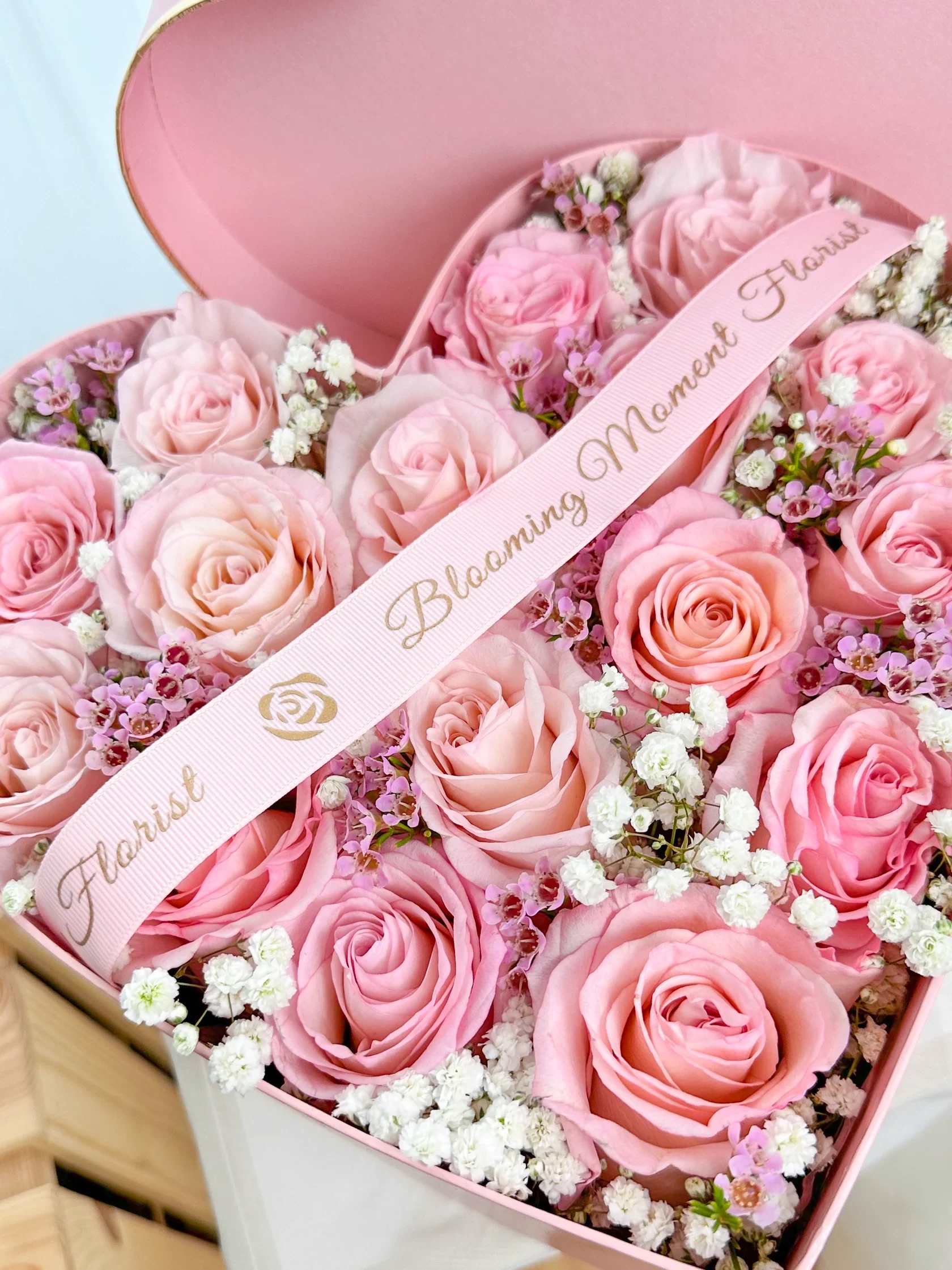 Pink roses arranged in a heart-shaped box with a ribbon