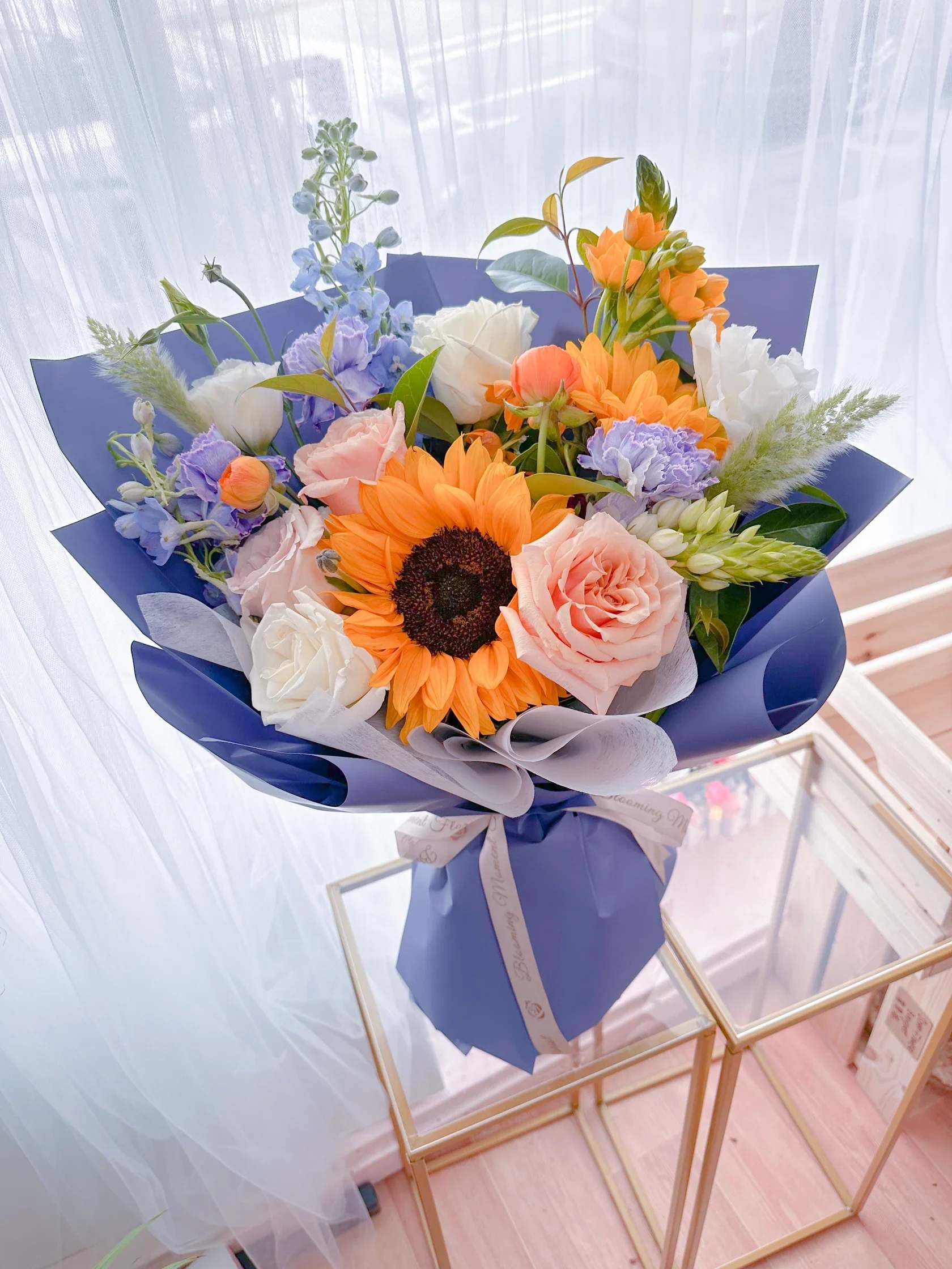 Bouquet of sunflowers, roses, and pastel flowers wrapped in blue paper