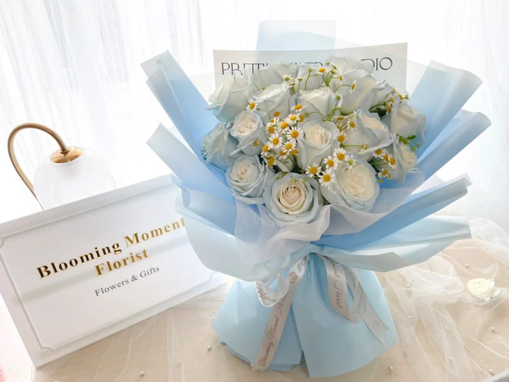 Bouquet of white roses and small daisies wrapped in pale blue paper
