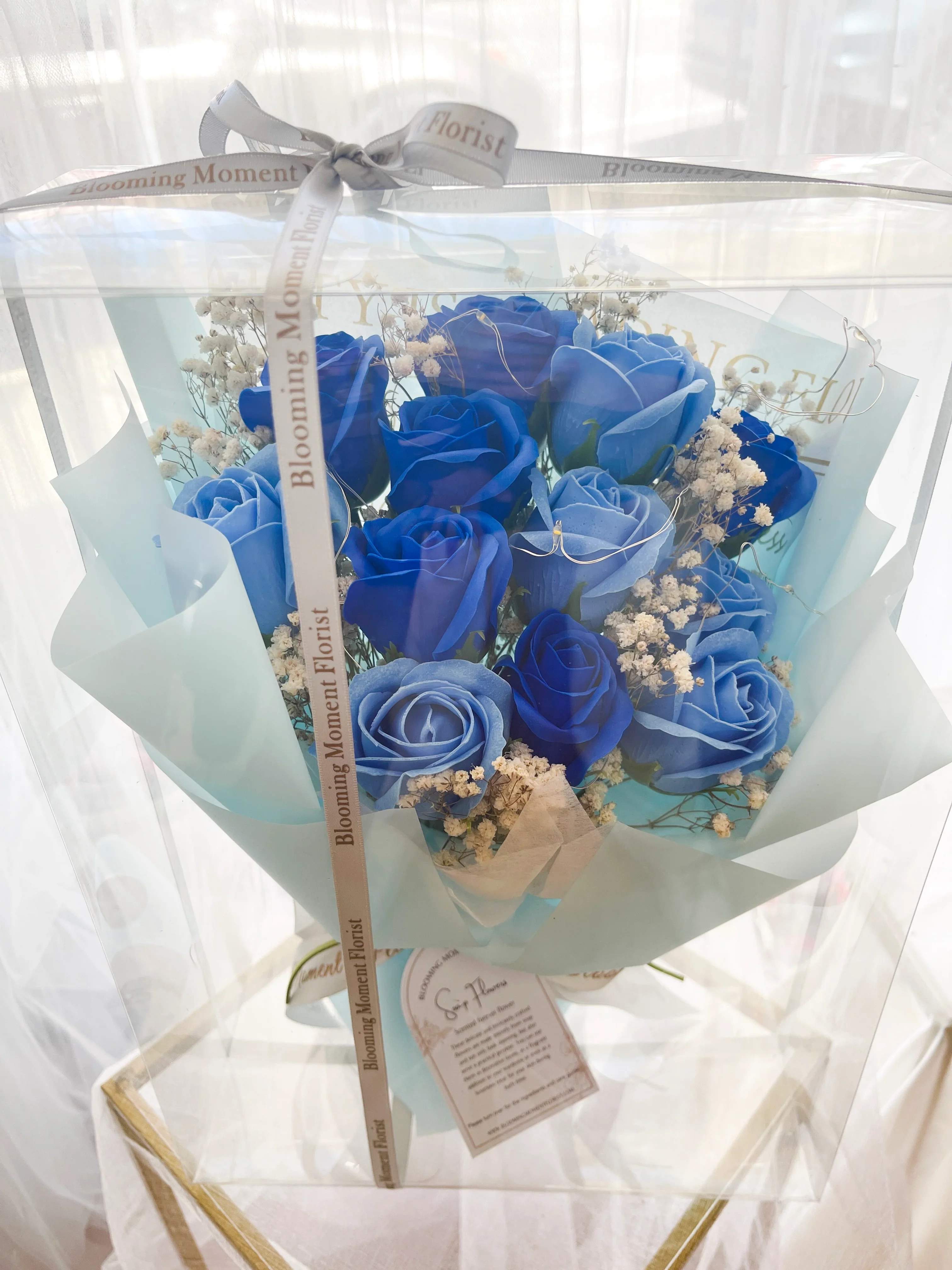 [SOAP FLOWER] Azure Glow Enchantment Soap Flower Bouquet - The Azure Glow Enchantment Soap Flower Bouquet features elegant blue and navy soap roses arranged in a clear display box and softly illuminated with warm LED lights for a romantic, glowing effect. This long-lasting soap flower arrangement is perfect as a Valentine’s Day gift, anniversary surprise, birthday present, or home décor piece.  Beautiful to display and lightly scented for bath use, it’s a unique floral gift that combines luxury, charm, and practicality — no watering needed.