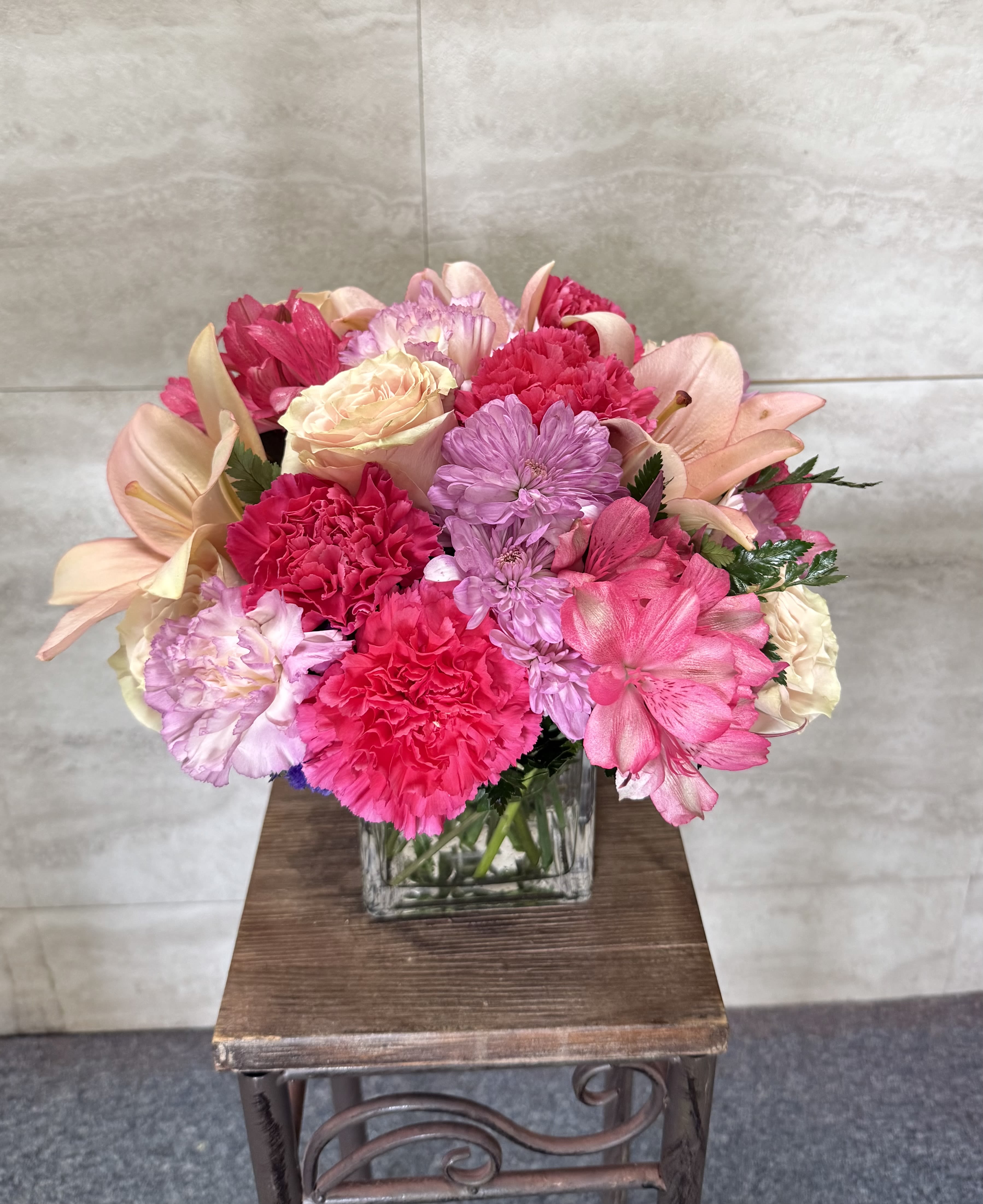 Ranpunzel - (ALL-ROUND) A cheerful, full arrangement of soft pinks and blush tones, featuring roses, carnations, alstroemeria, and mums, beautifully gathered in a clear glass cube for a fresh, elegant look. 