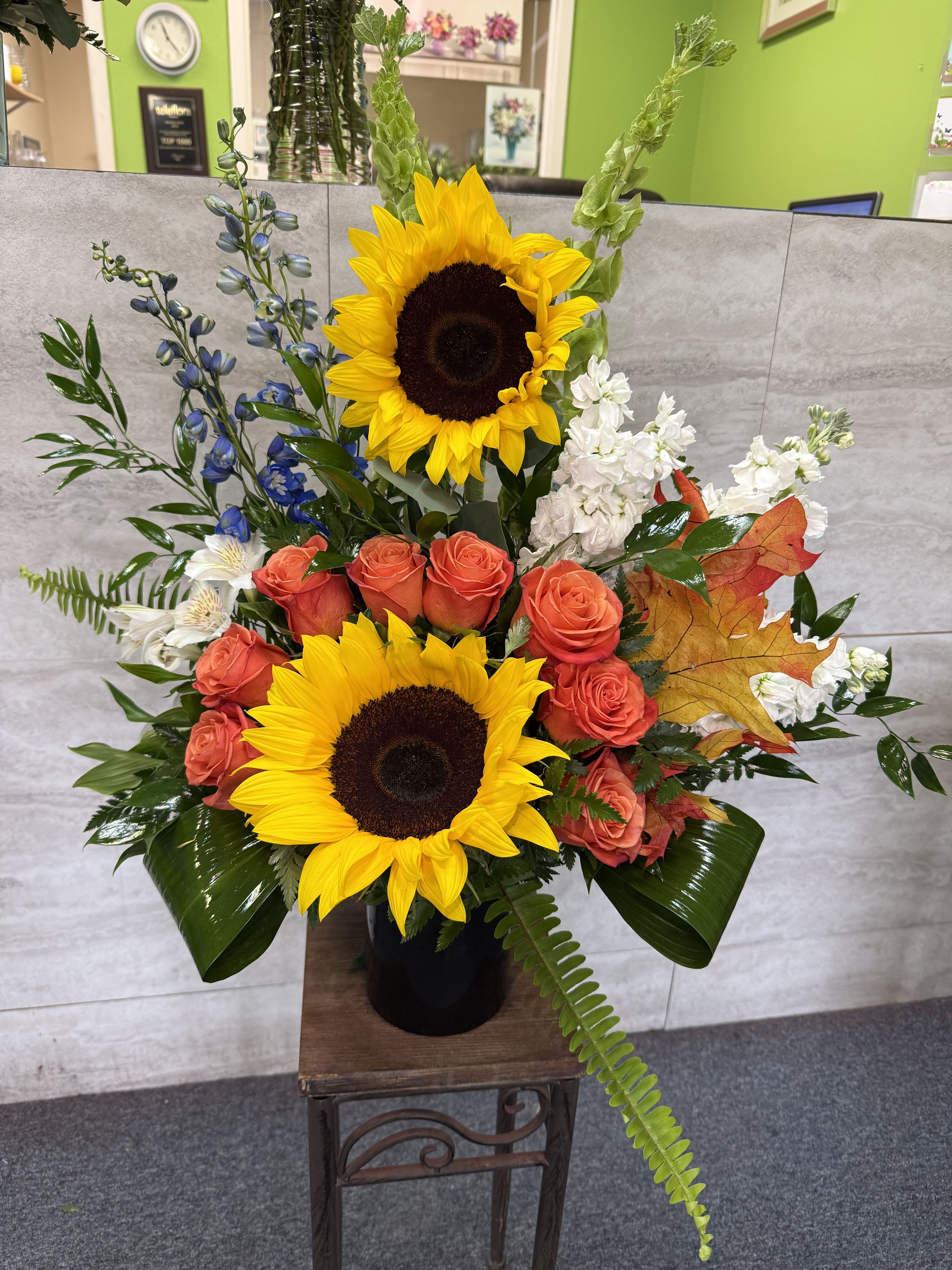 Tall floral arrangement with sunflowers, coral roses, and white blooms in a black vase