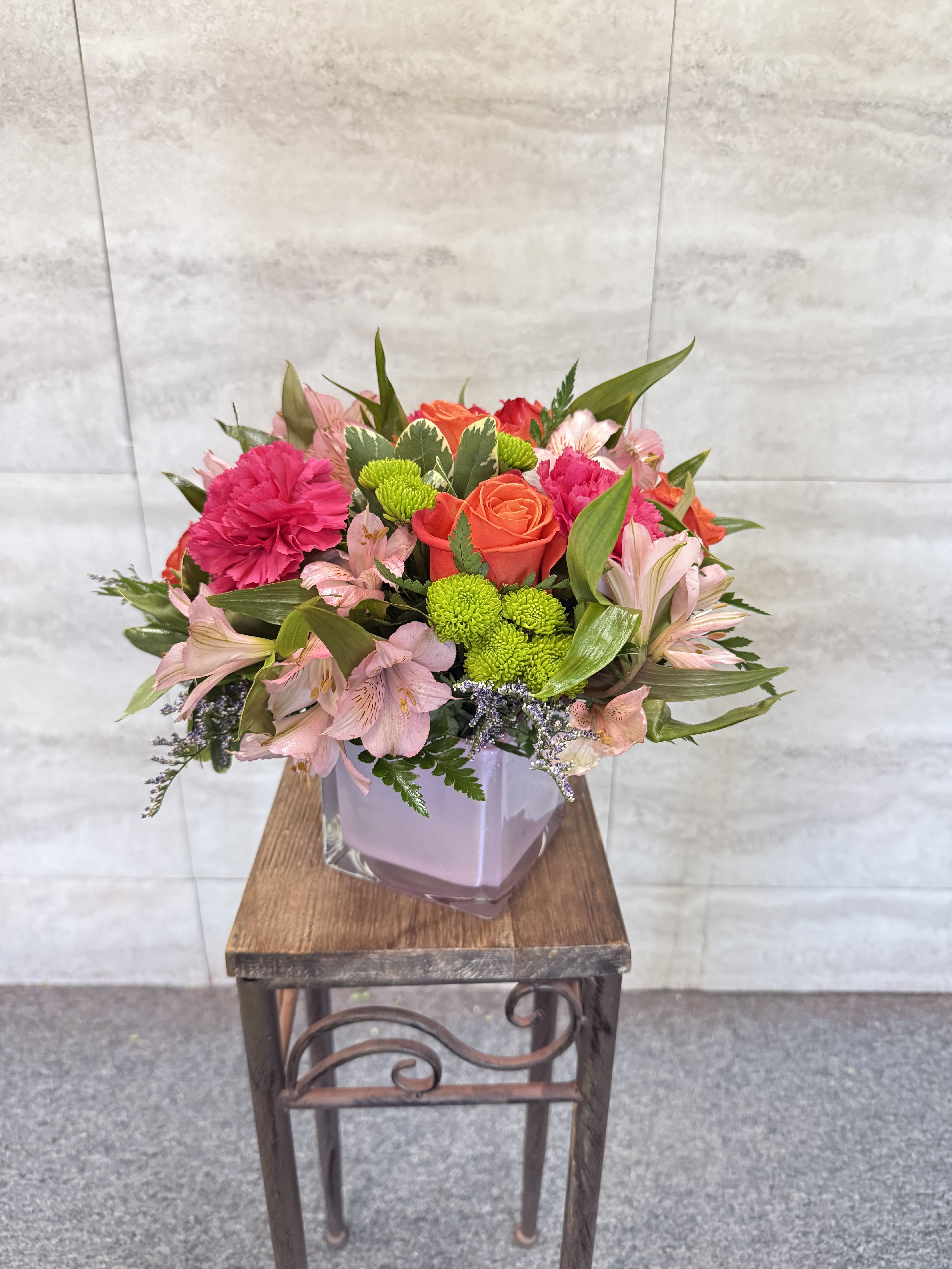 Mixed pink and orange flowers arranged in a square glass vase