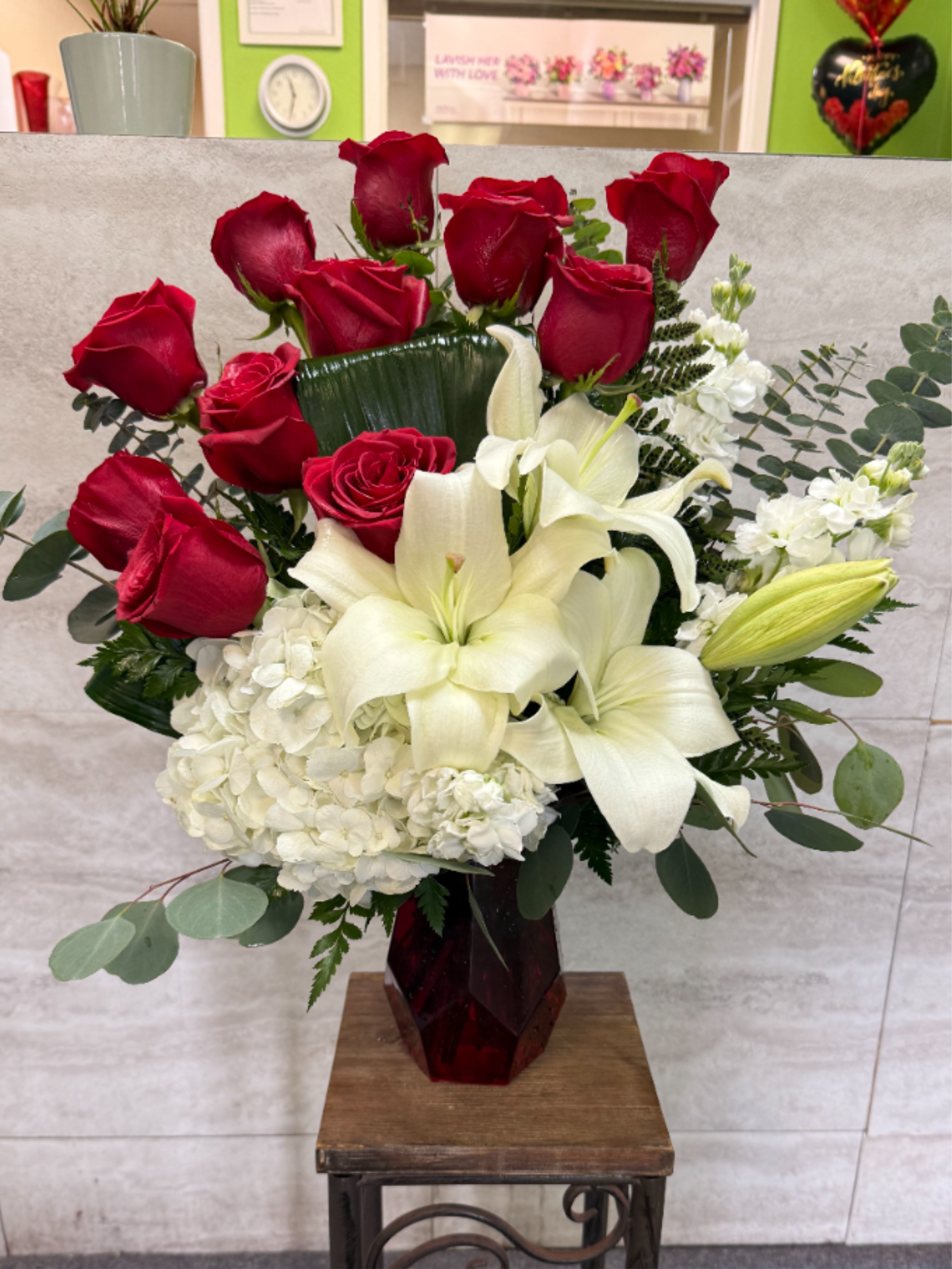 Tall arrangement of red roses, white lilies, and white hydrangeas in a red glass vase