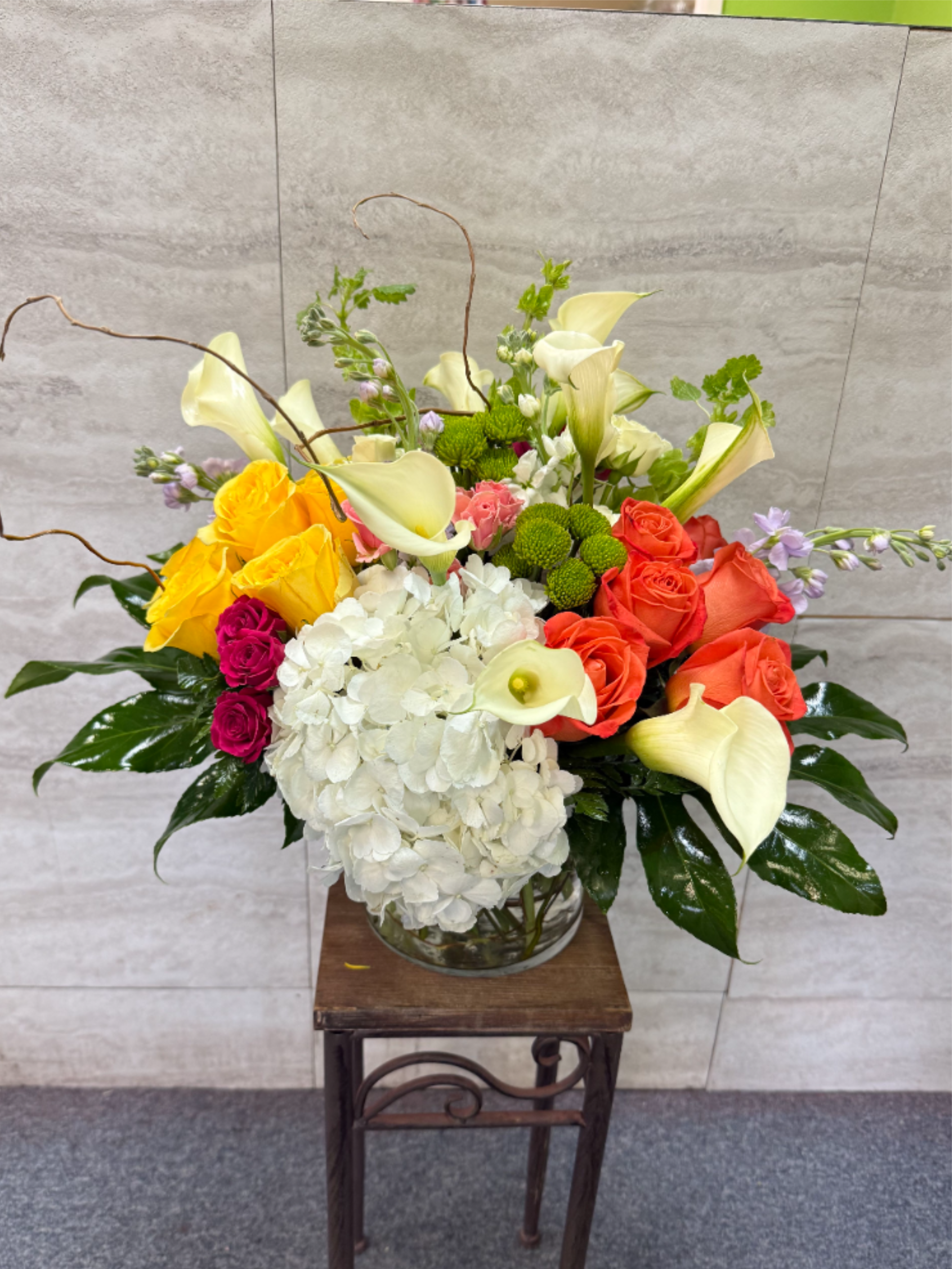 Citrus Garden Elegance - (ONE-SIDED) A vibrant blend of golden yellow and coral roses, creamy calla lilies, and a lush white hydrangea centerpiece, accented with playful pops of green and delicate florals. This arrangement feels fresh, bright, and effortlessly elegant — perfect for making a statement.