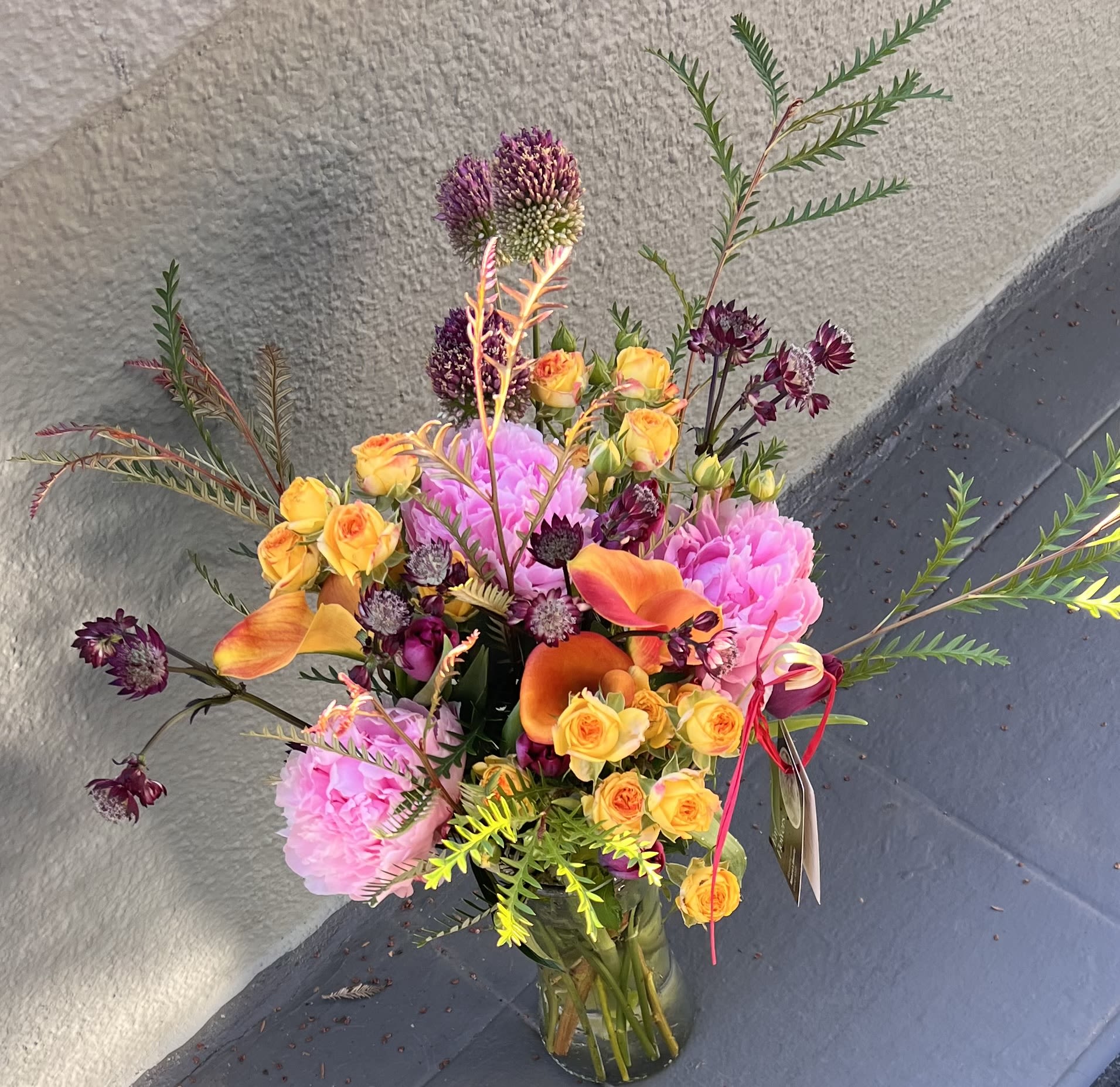 Sunset Garden  -  A vibrant, garden-style arrangement bursting with color and texture. This bouquet features lush pink peonies, clusters of golden-yellow spray roses, and striking orange calla lilies that add warmth and depth.  