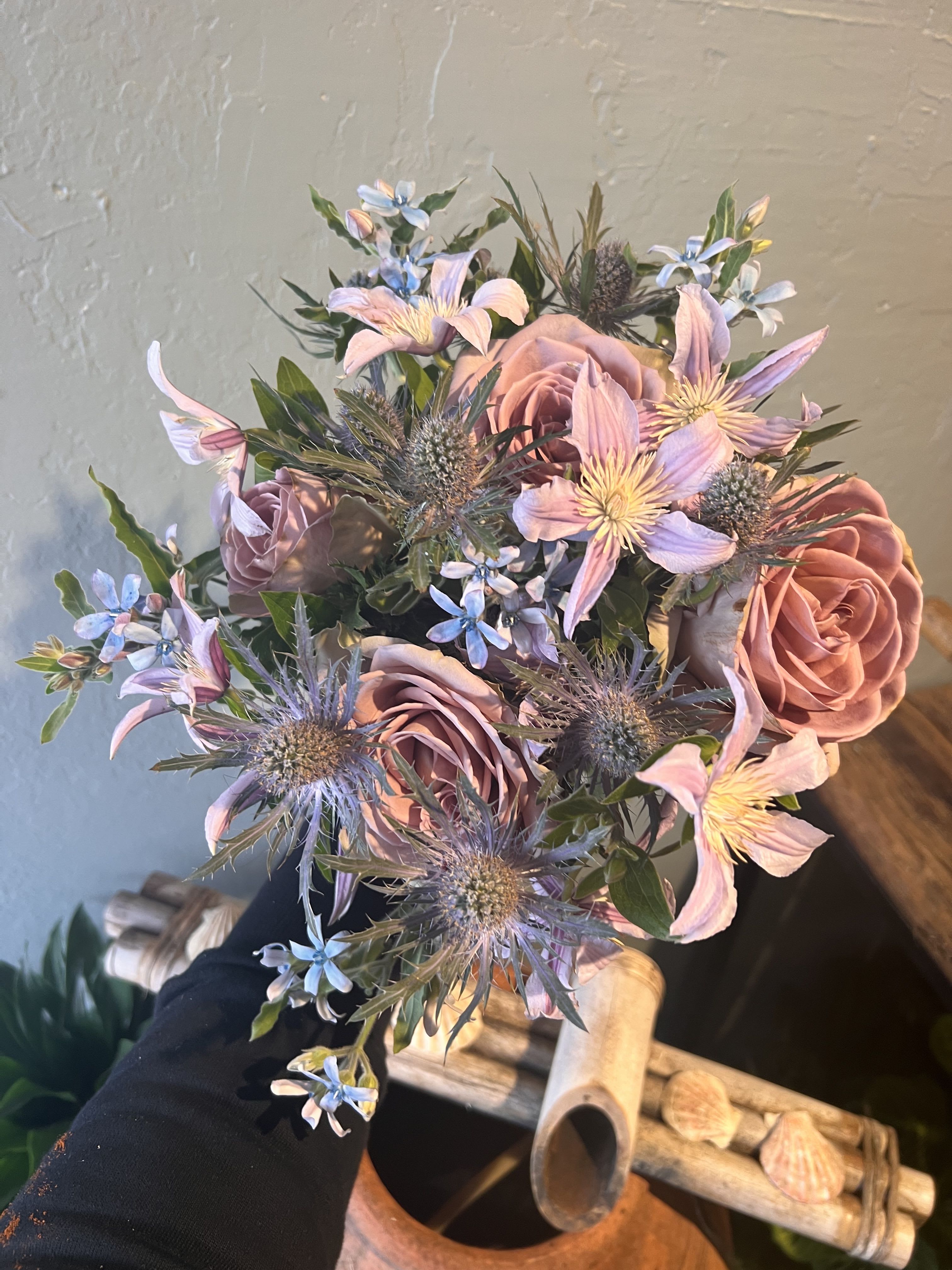 Lavender Dusk  - A couture palette of dusty mauve roses, lilac clematis, and cool blue thistles, composed with the elegance of a fine-art still life. Each stem is placed with intentional grace, creating movement and depth that whisper sophistication. Designed for those who appreciate beauty that doesn’t beg for attention — it arrives like a secret, confident and unforgettable.