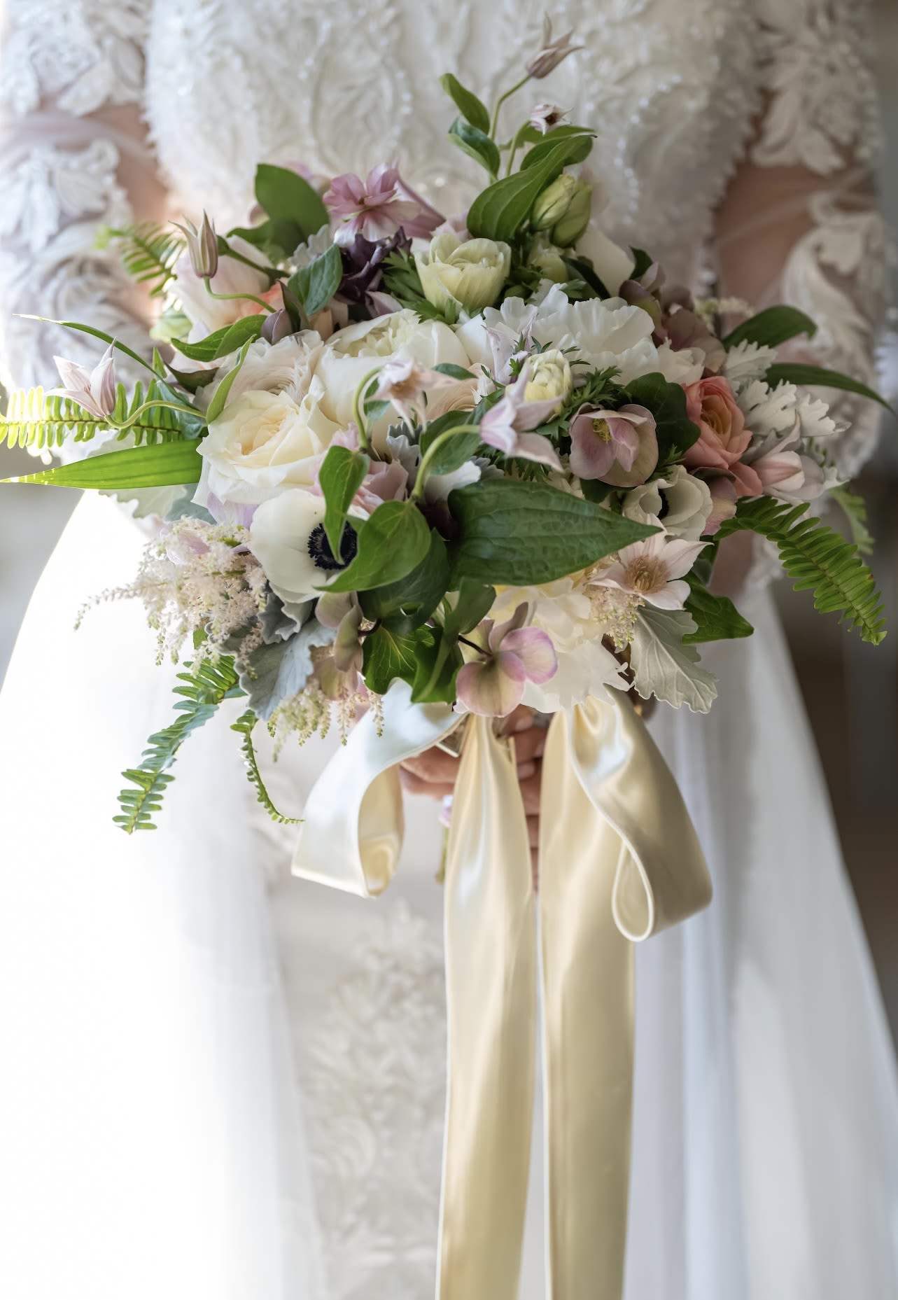  Silk-Tied Reverence bridal bouquet  - A soft garden–inspired bridal bouquet designed for the modern romantic. Filled with ivory and blush roses, delicate anemones, hellebores, and sweet textural blooms, this piece feels like a walk through an enchanted spring garden. Wisps of greenery and a champagne satin ribbon finish the design with effortless elegance — perfect for brides who want their flowers to feel timeless, feminine, and deeply sentimental.