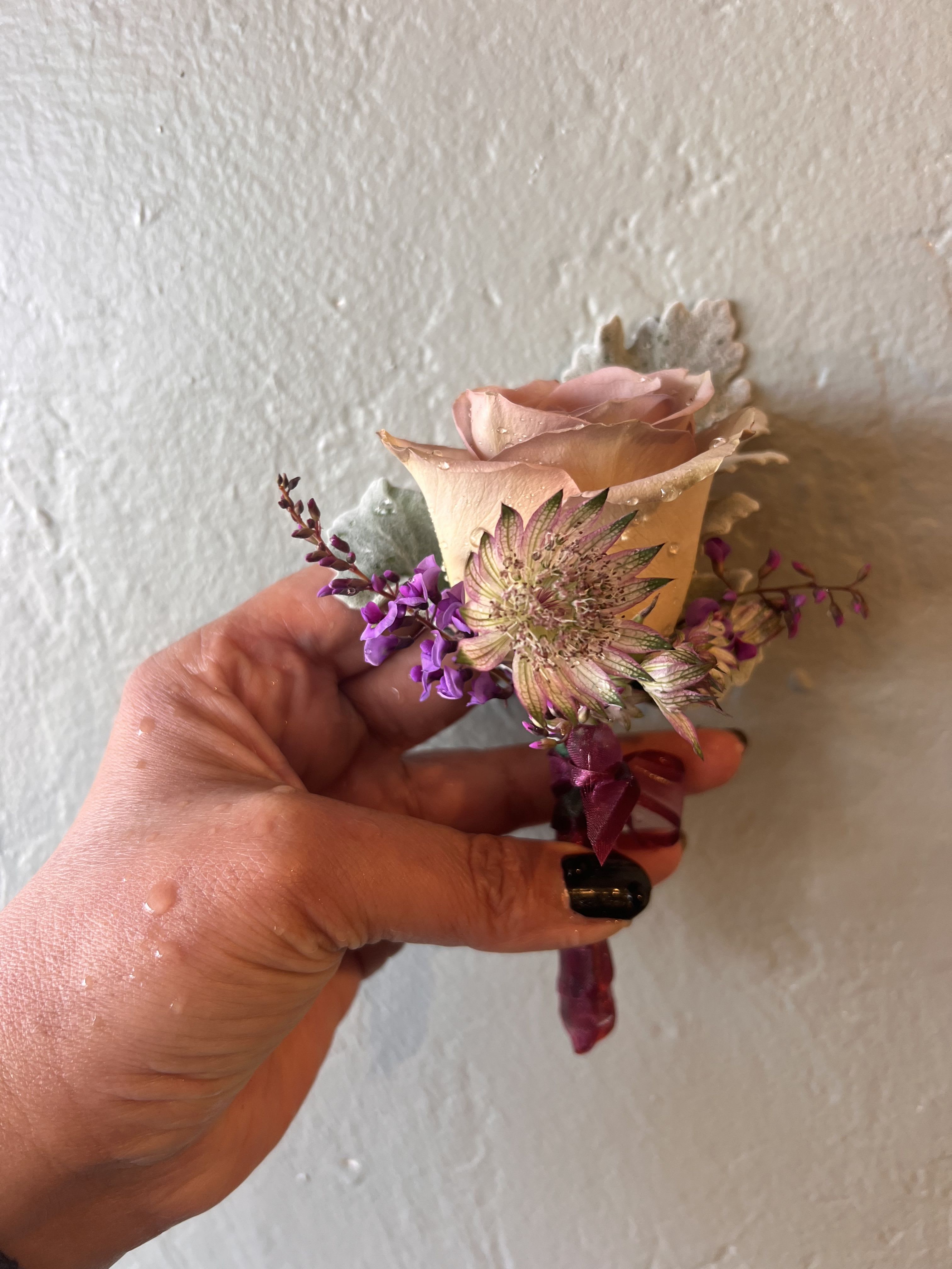 Blush Whisper Boutonniere - The Blush Whisper Boutonniere features a soft blush rose accented with delicate seasonal blooms and refined textural greenery. Handcrafted with care, this timeless piece adds a subtle touch of romance and sophistication to any formal look.  Perfect for weddings, proms, homecoming, formal dances, engagement parties, anniversaries, quinceañeras, graduations, galas, and black-tie events. Ideal for grooms, groomsmen, prom dates, and anyone seeking an elegant floral accent.